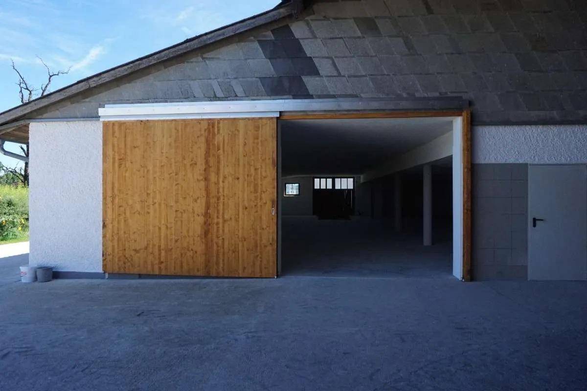 Außenansicht eines großen Holzschiebetors an einem Gebäude, das in einen dunklen Innenraum führt.