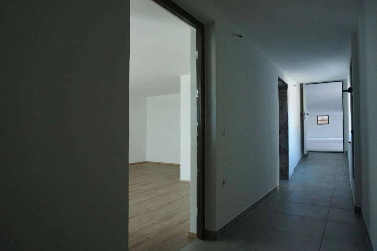 Heller Flur mit grauen Fliesen und weißen Wänden, der zu einem Raum mit Holzlaminatboden führt.