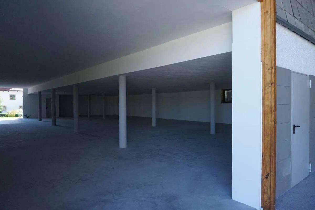 Weiter Blick in einen großen, leeren Innenraum mit Betonboden, weißen Wänden und vielen tragenden Säulen.