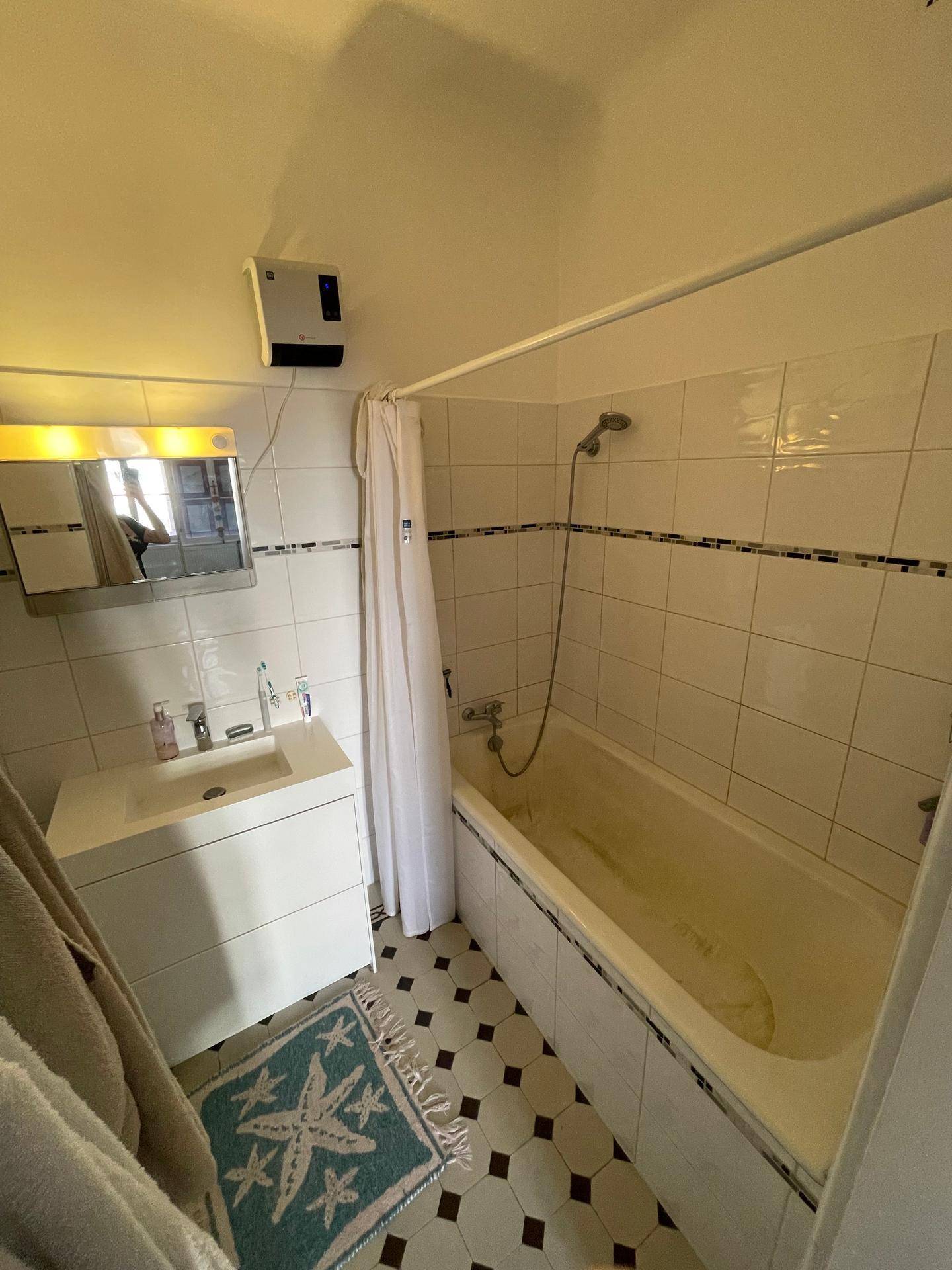 Badezimmer mit Badewanne, Duschvorhang und schwarz-weiß gemusterten Bodenfliesen.