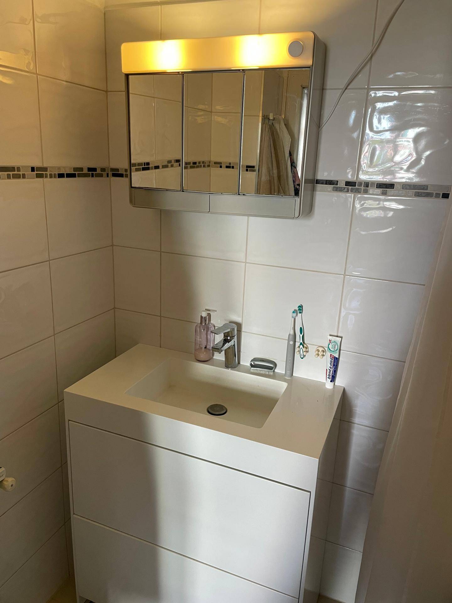 Modernes Badezimmer mit weißem Waschtisch, Spiegelschrank und hellen Fliesen.