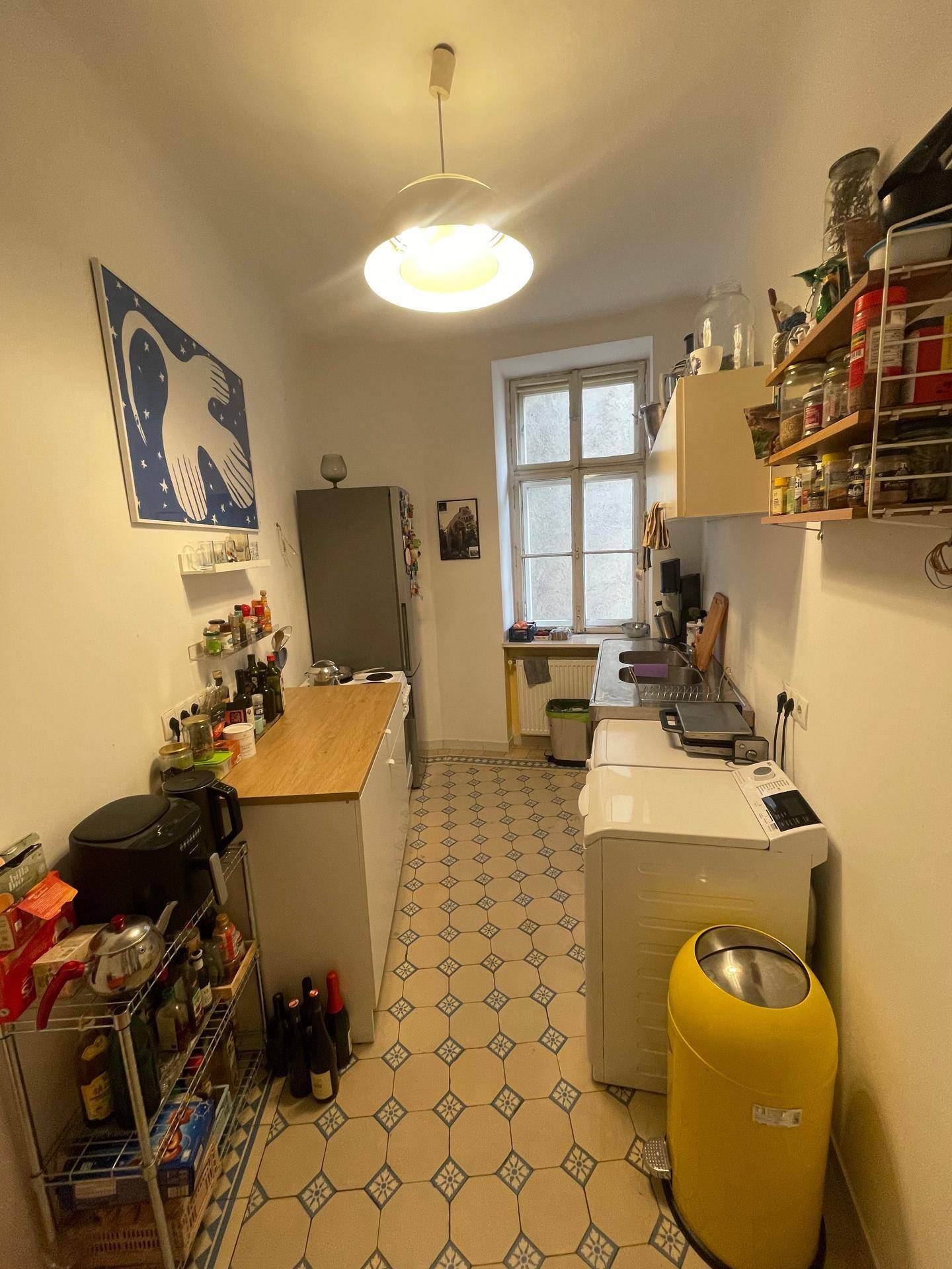 Schmale Küche mit gemusterten Bodenfliesen, Fenster und funktionaler Einrichtung.