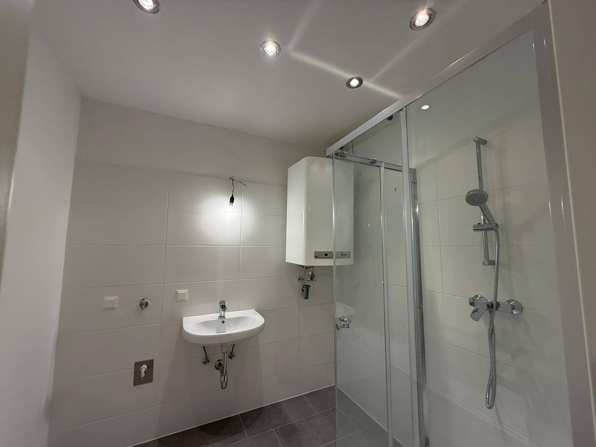 Funktionales Badezimmer mit Dusche, Waschbecken und Wandboiler, komplett gefliest.