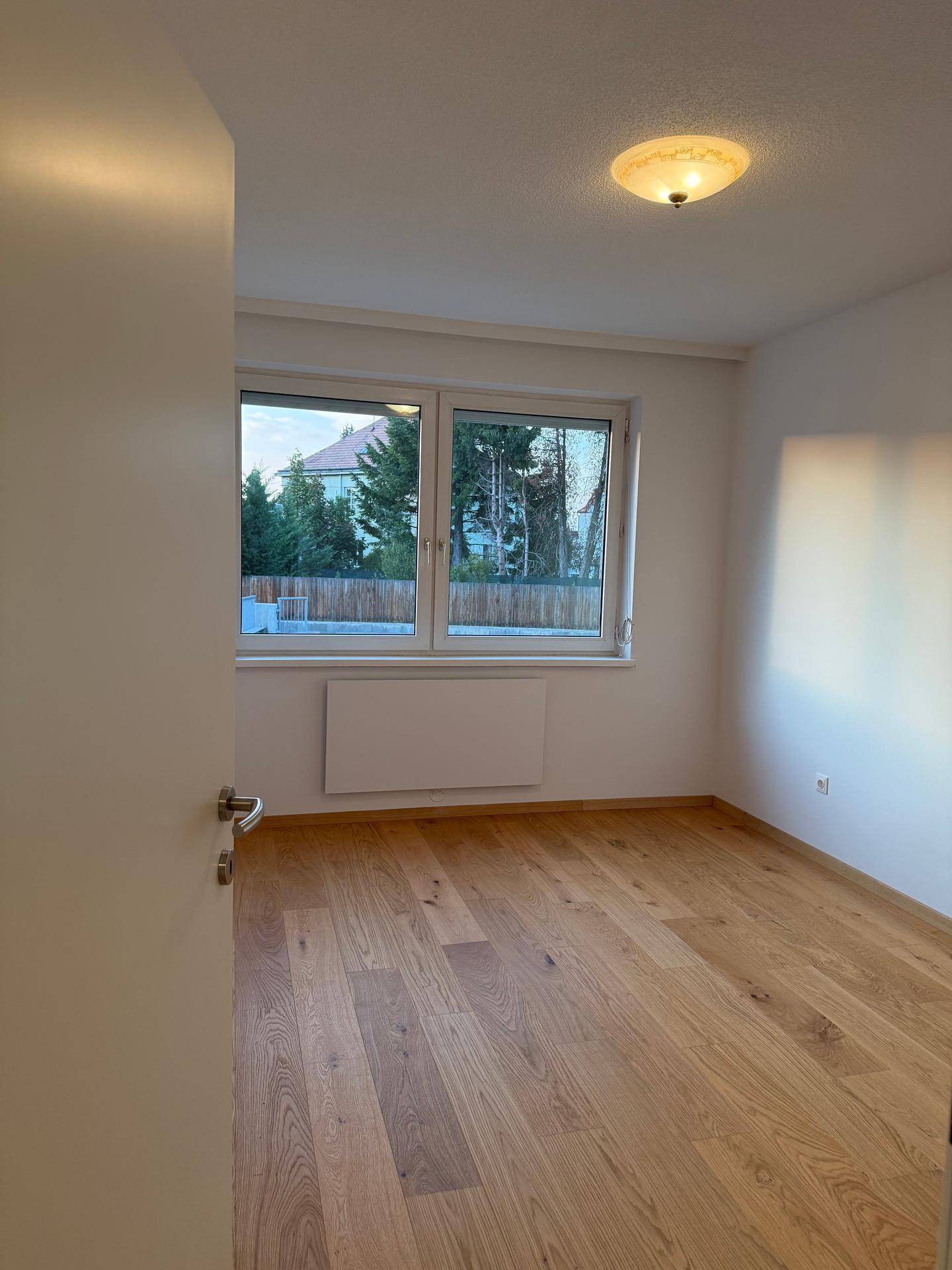 Helles Schlafzimmer mit Holzparkettboden und einem Fenster, das einen Blick ins Grüne bietet.