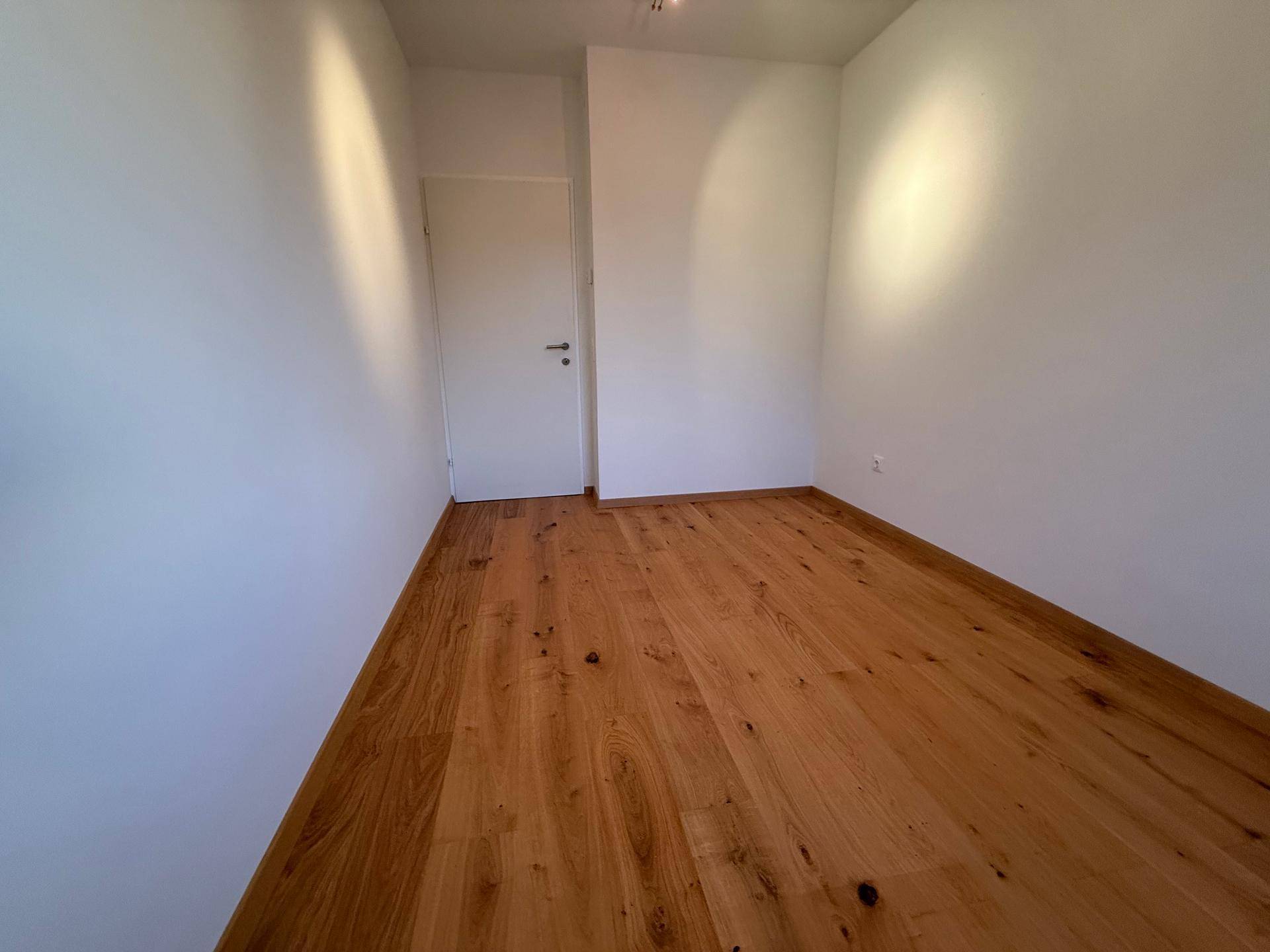 Unmöbliertes Zimmer mit Holzparkettboden und weißen Wänden, ideal als Schlaf- oder Arbeitszimmer.
