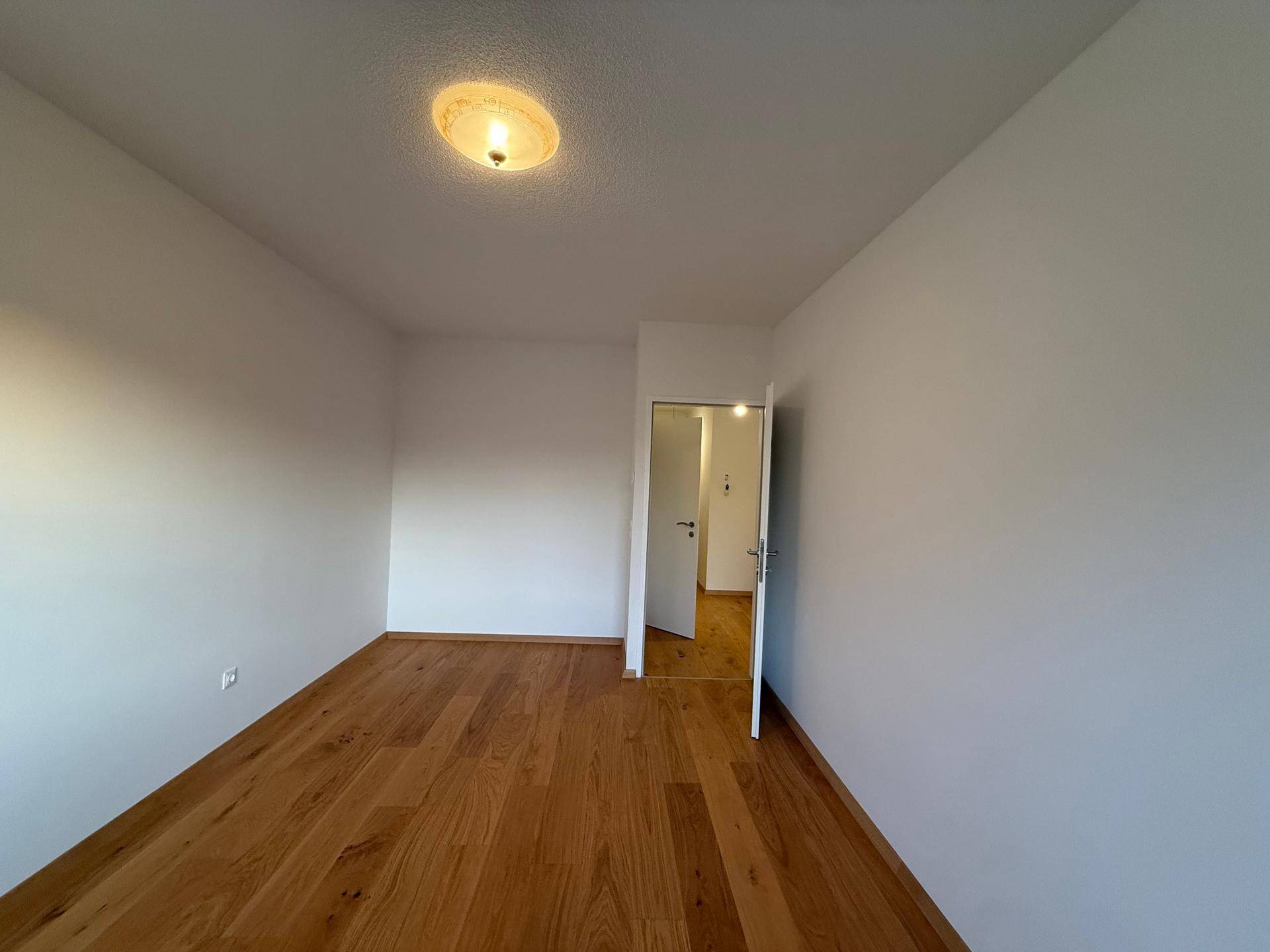Leeres Zimmer mit hellem Holzparkett und weißen Wänden, bereit zur individuellen Gestaltung.