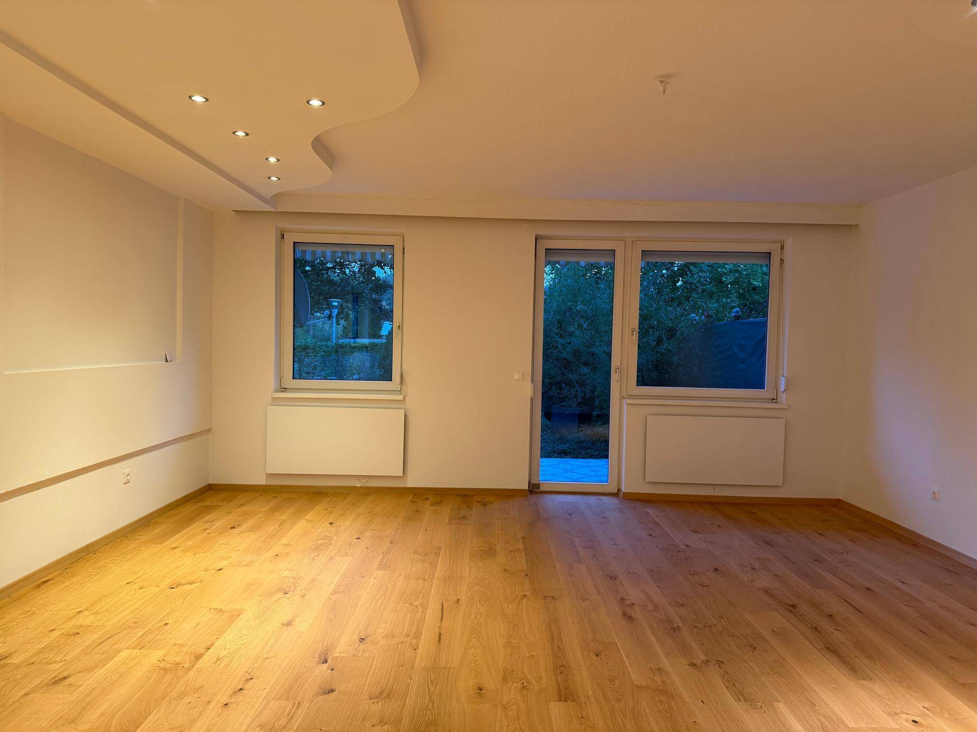 Heller Wohnbereich mit Holzparkettboden und großen Fenstern, die Zugang zur Terrasse bieten.