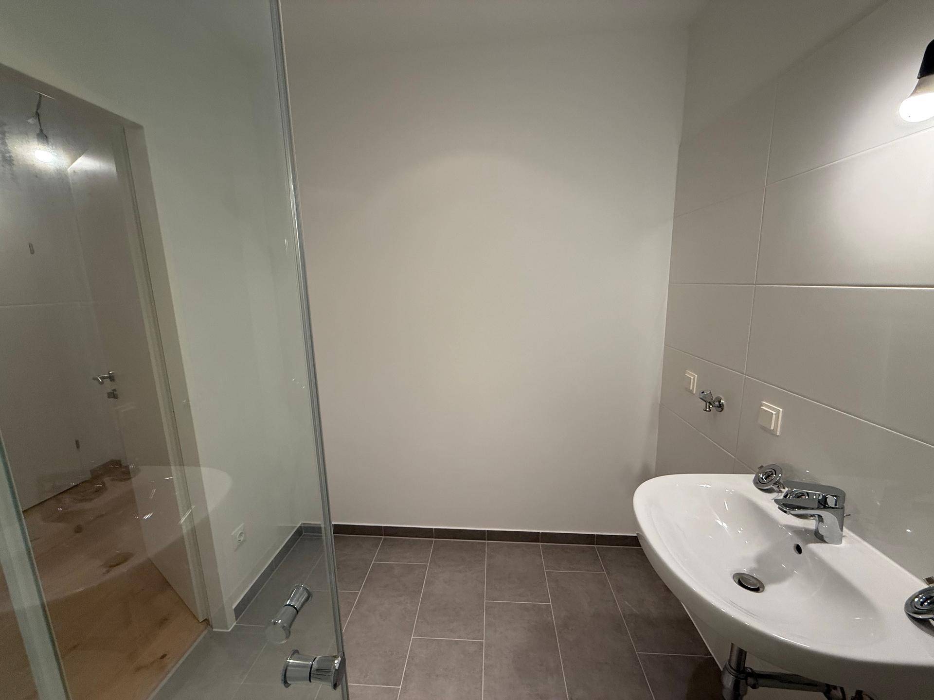 Modernes Badezimmer mit Waschbecken, Duschbereich und grauen Bodenfliesen.
