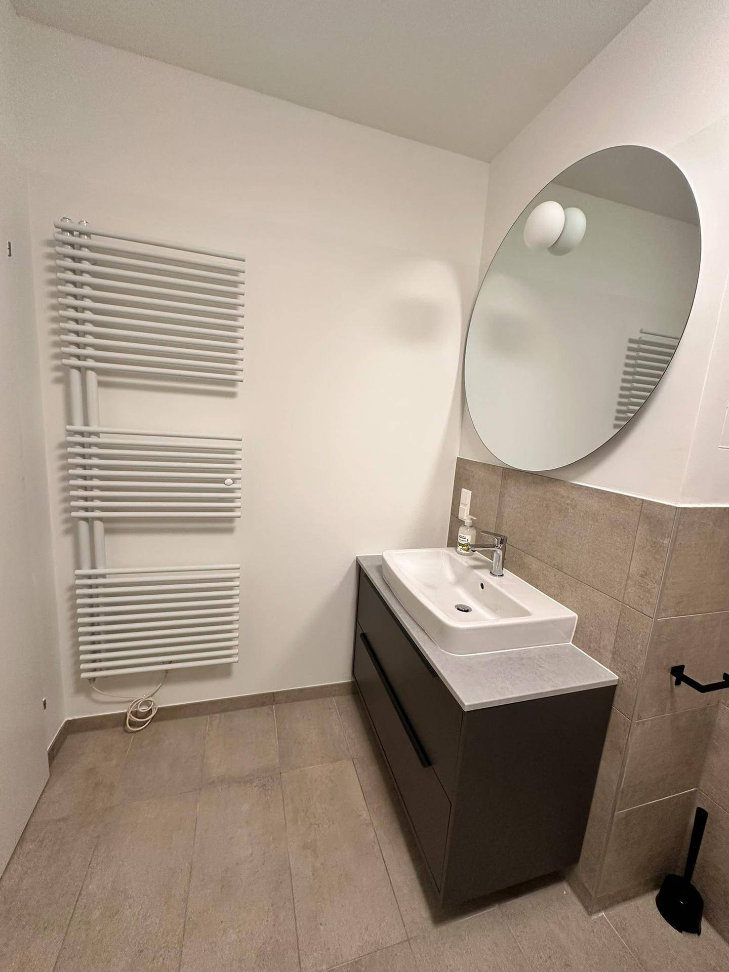 Badezimmer mit modernem Waschtisch, großem Spiegel und praktischem Handtuchheizkörper.