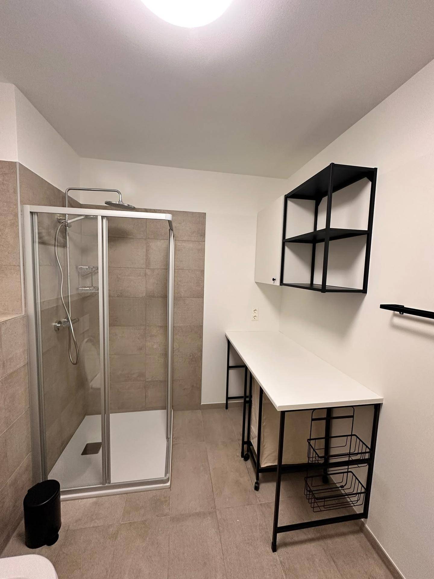 Funktionaler Bereich im Badezimmer mit Dusche und praktischer Arbeitsfläche sowie Regalen.