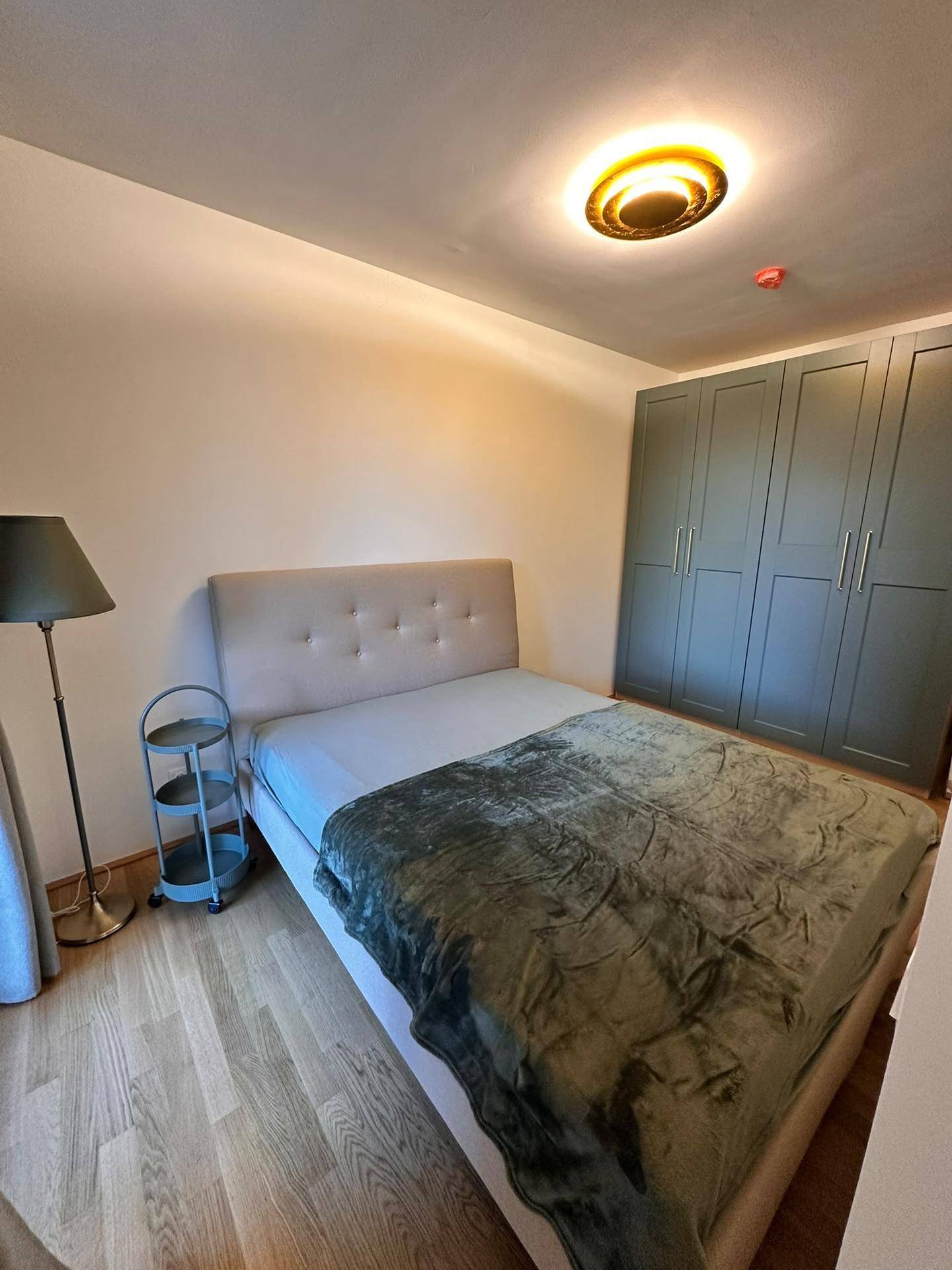 Schlafzimmer mit großem Kleiderschrank, beigem Bett und Holzboden, hell beleuchtet.