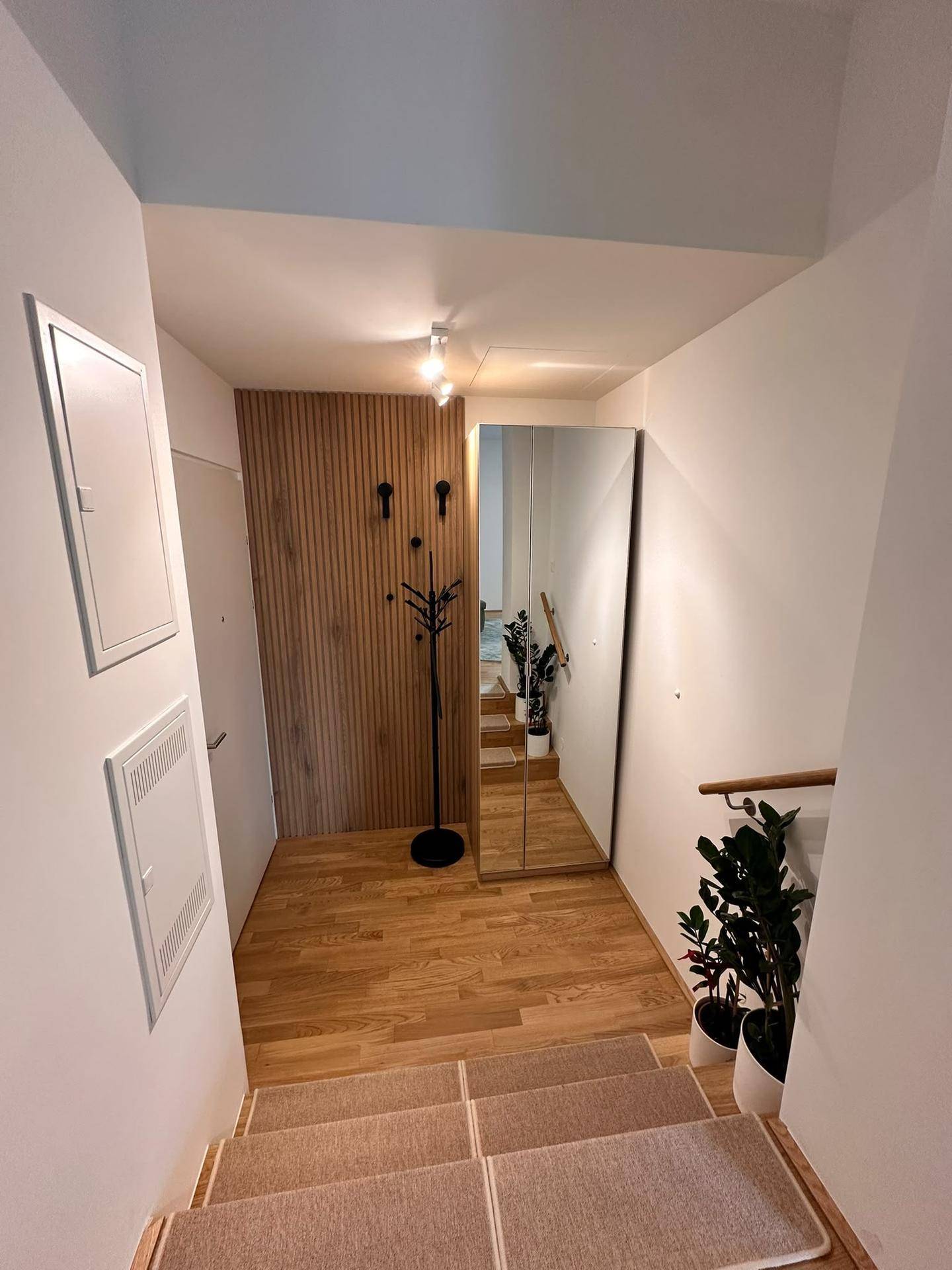 Heller Eingangsbereich mit Holzvertäfelung, großem Spiegel und Treppe zum oberen Stockwerk.