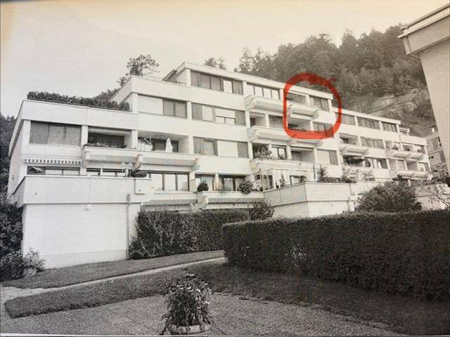 Mehrfamilienhaus mit gestufter Architektur und zahlreichen Balkonen vor bewaldetem Hang.