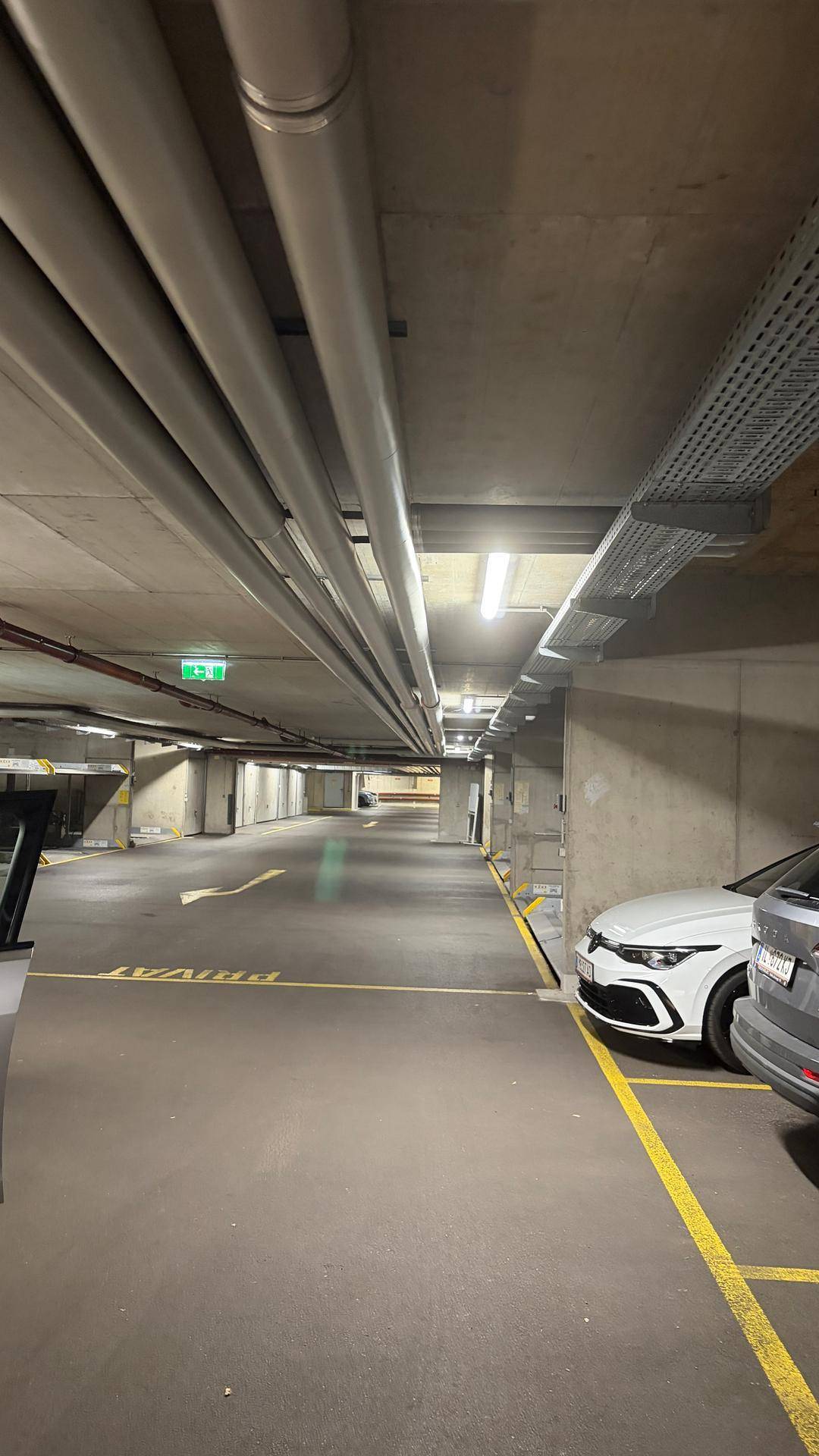 Geräumige Tiefgarage mit mehreren Stellplätzen, sichtbaren Leitungen und guter Beleuchtung.