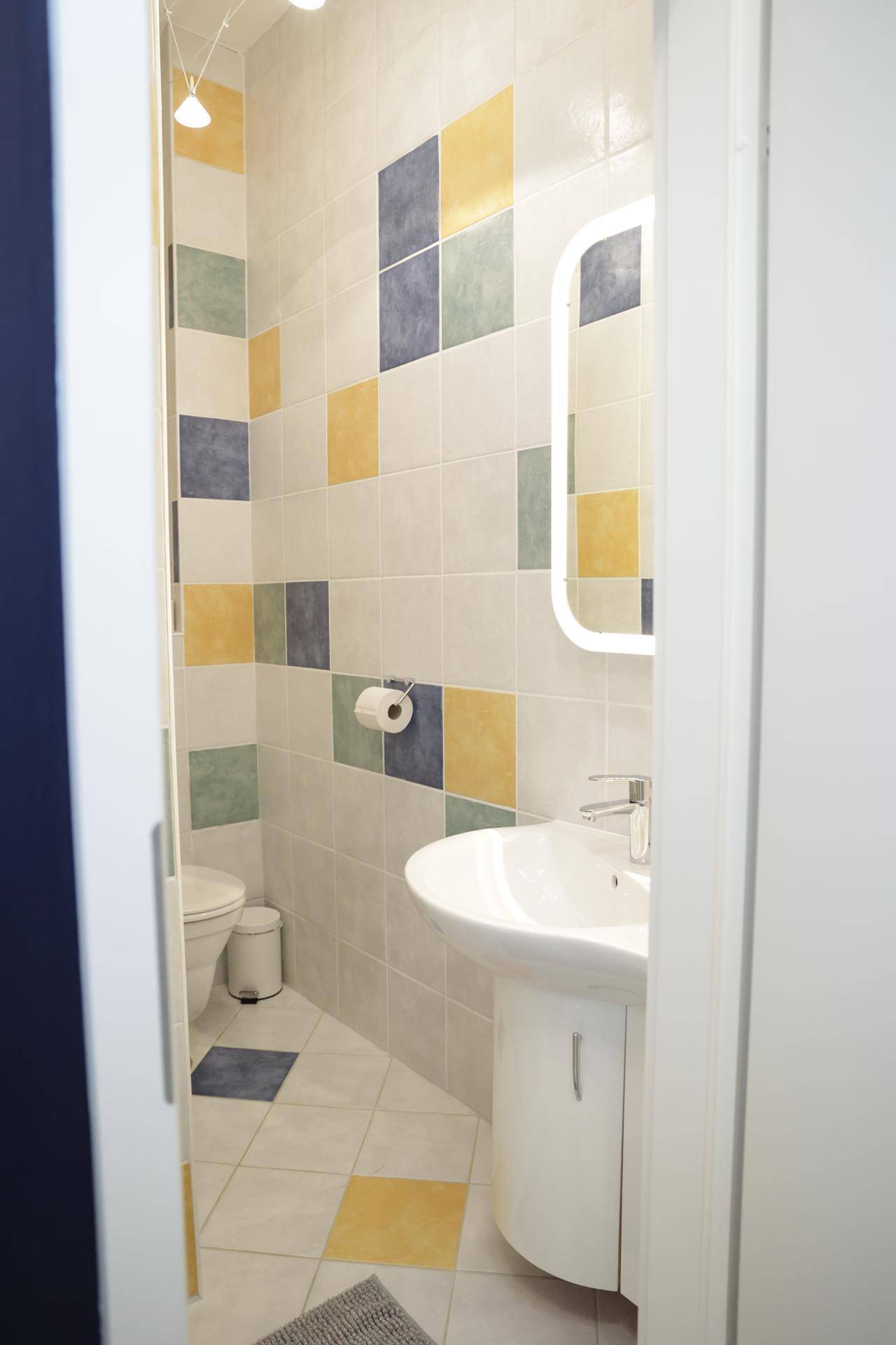Kleines WC mit farbigen Fliesen, Waschbecken und Spiegel.