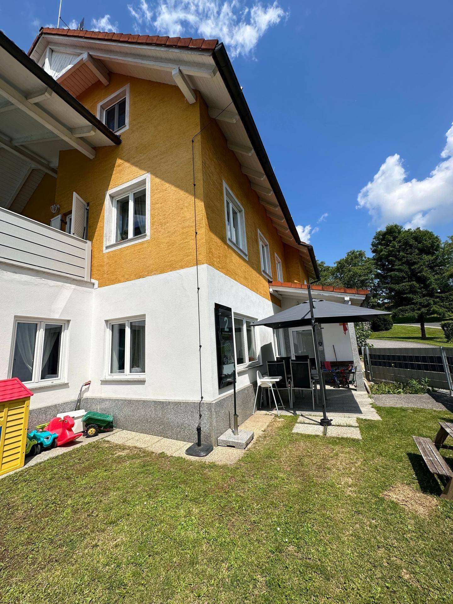 Gartenbereich des Hauses mit Rasenfläche, Sonnenschirm und Kinderspielzeug.