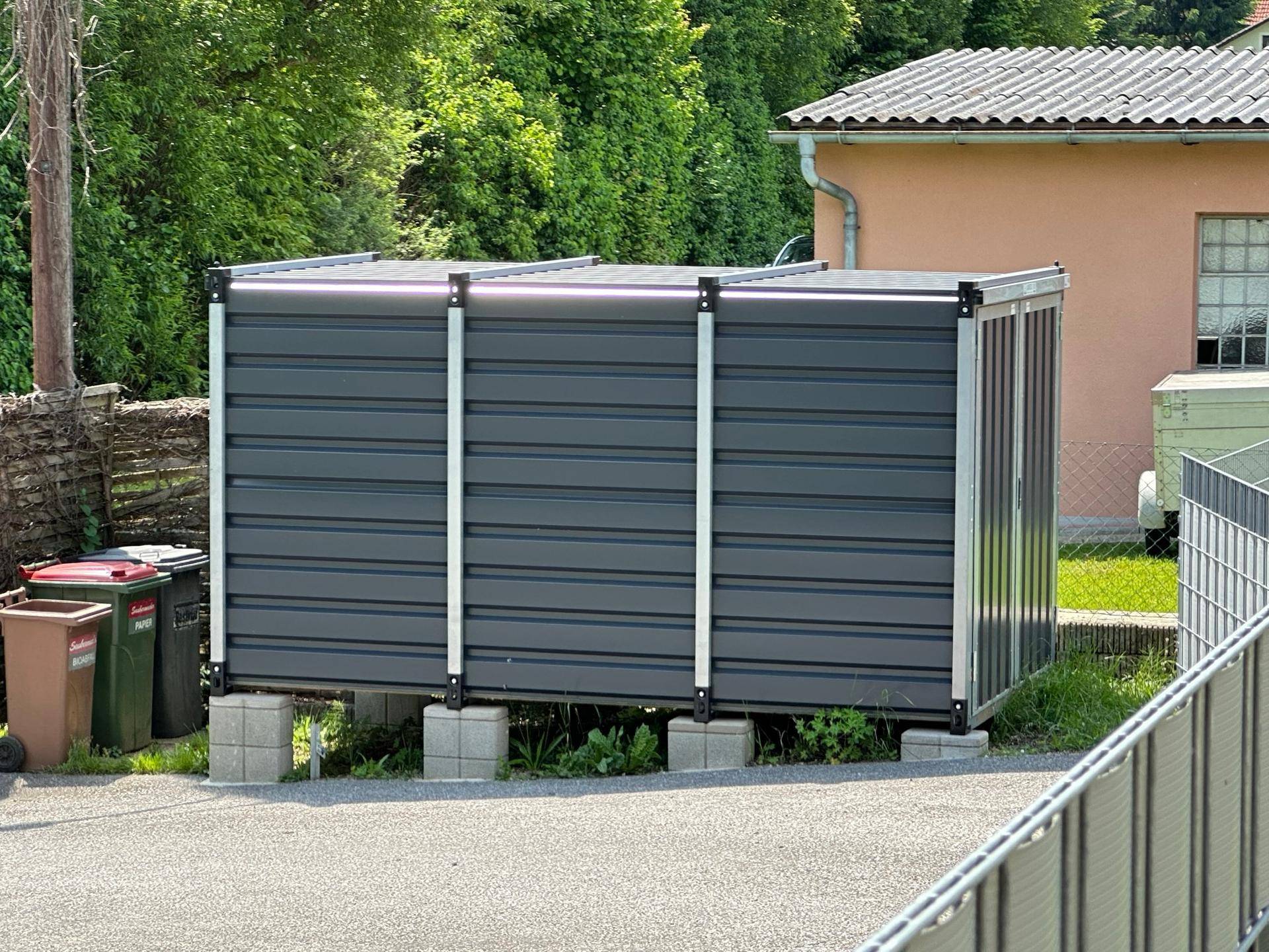 Moderner, grauer Geräteschuppen im Außenbereich auf Betonfundamenten.