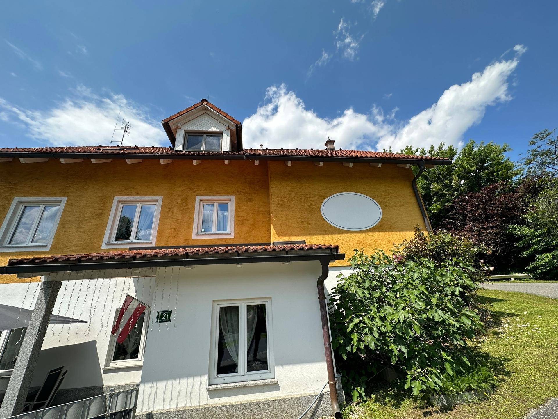 Seitenansicht des gelb verputzten Hauses mit roten Dachziegeln und mehreren Fenstern.