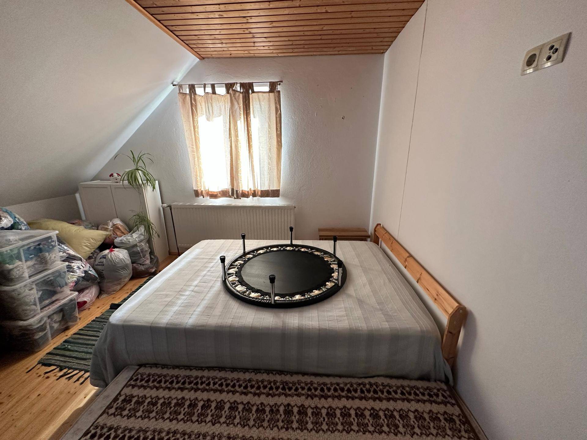 Helles Schlafzimmer im Dachgeschoss mit Holzbalkendecke, Fenster und einem Trampolin auf dem Bett.
