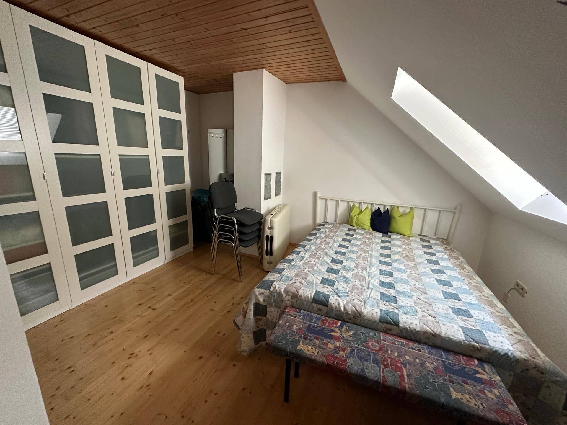 Gemütliches Schlafzimmer im Dachgeschoss mit Holzbalkendecke, Einbauschränken und Dachfenster.