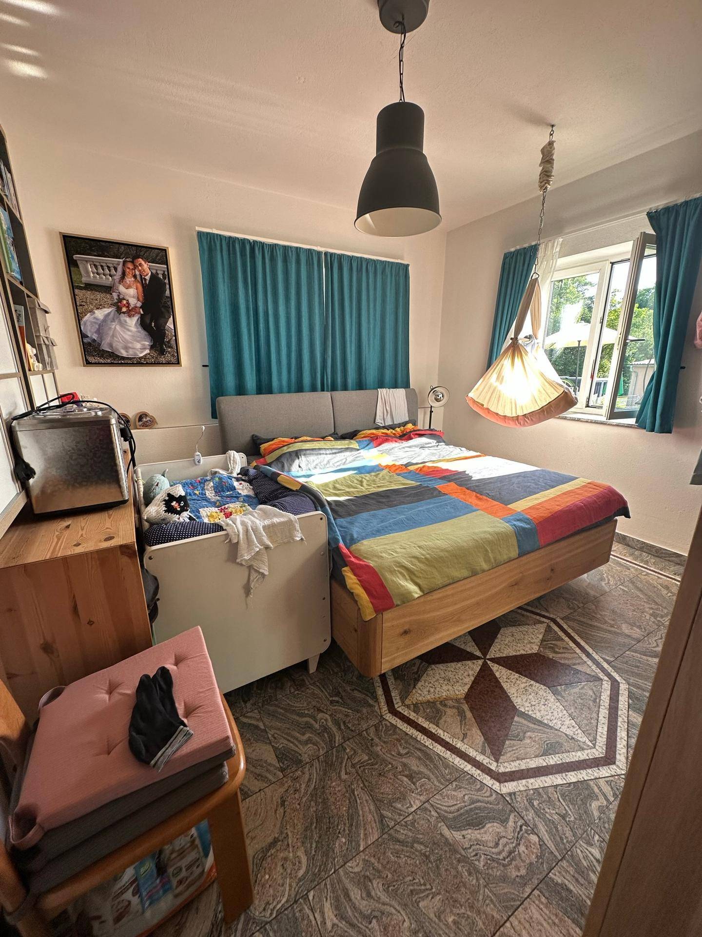 Helles Schlafzimmer mit Doppelbett, blauen Vorhängen und auffälligem Fliesenbodenmuster.