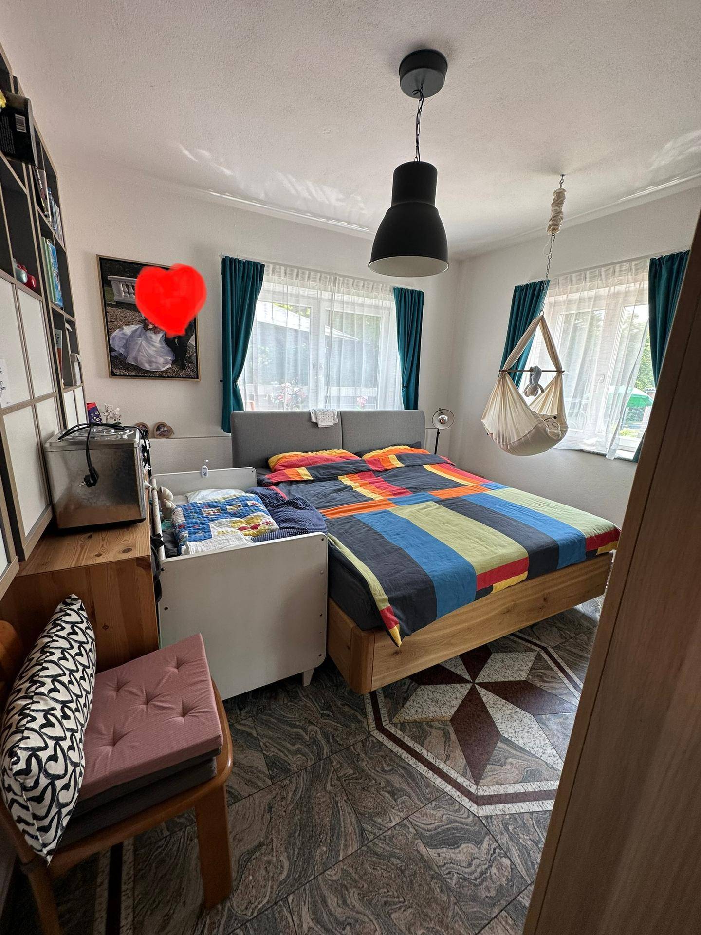 Schlafzimmer mit Doppelbett, gemustertem Boden und Hängesessel am Fenster.
