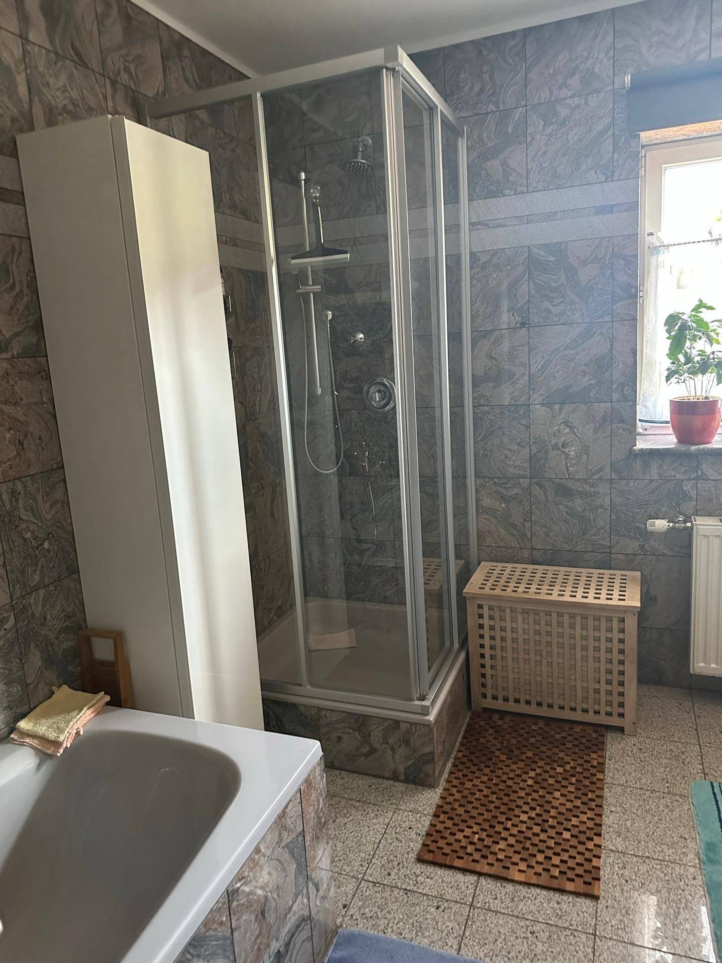 Badezimmer mit Duschkabine, Badewanne und gefliesten Wänden und Böden.