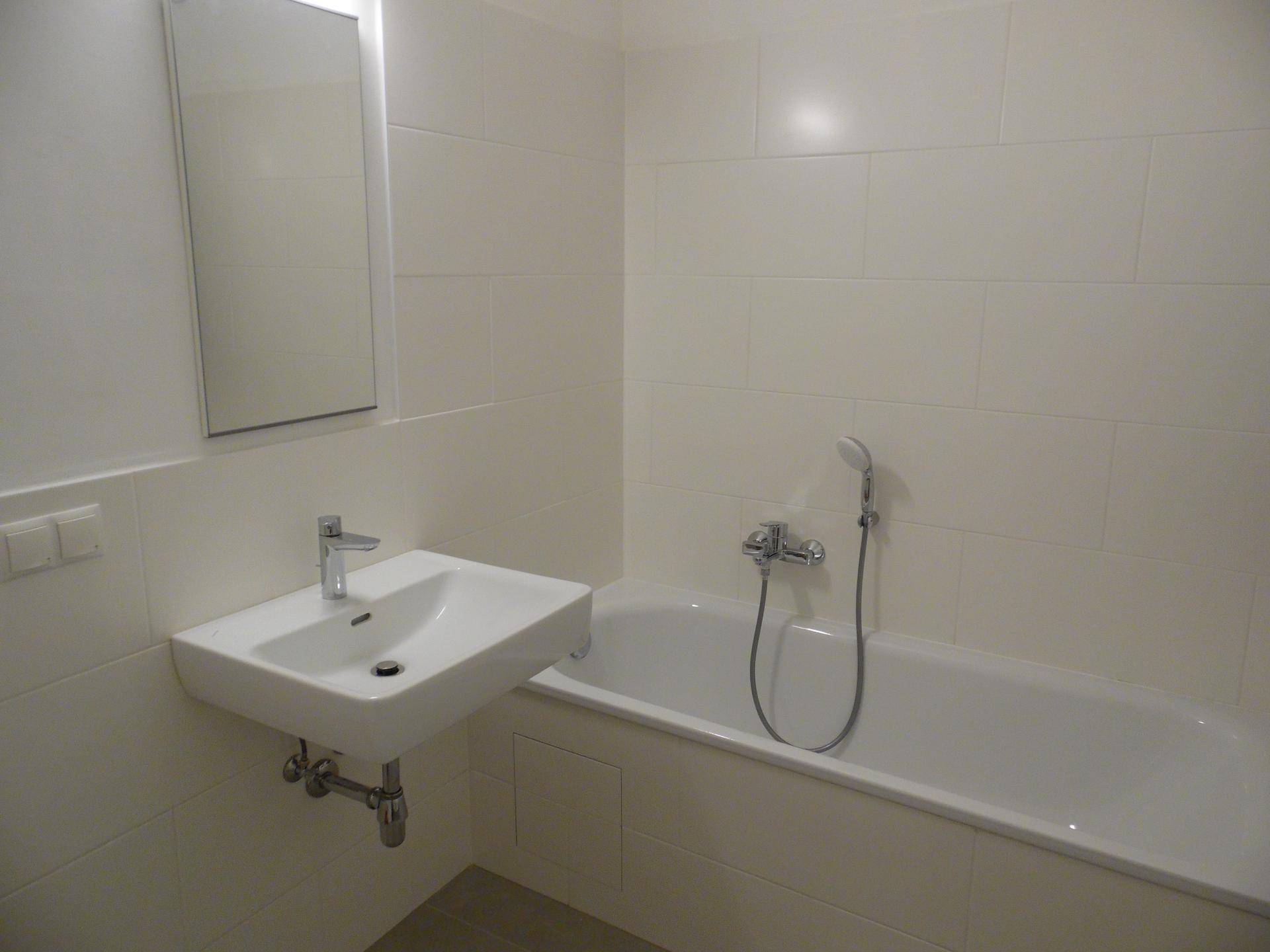 Modernes Badezimmer mit weißen Fliesen, Waschbecken und einer Badewanne mit Duschfunktion.