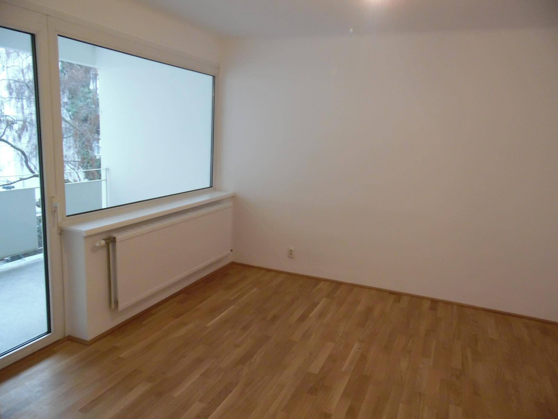 Lichtdurchflutetes Zimmer mit Parkettboden und Zugang zu einem Balkon, mit Blick ins Grüne.