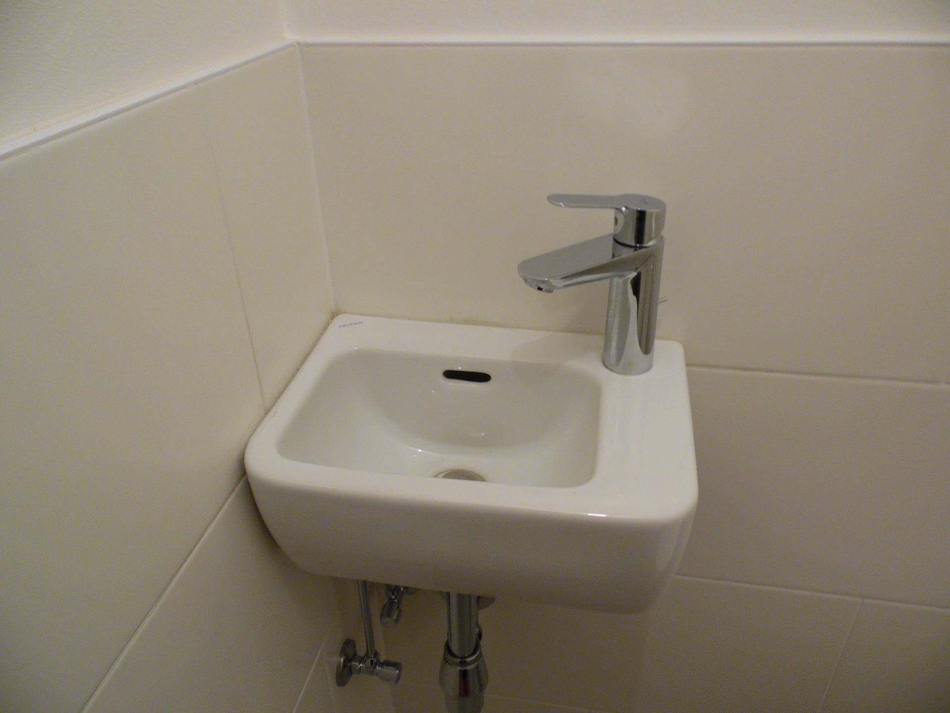 Kleines, funktionales Gäste-WC mit einem kompakten Waschbecken und weißen Fliesen.
