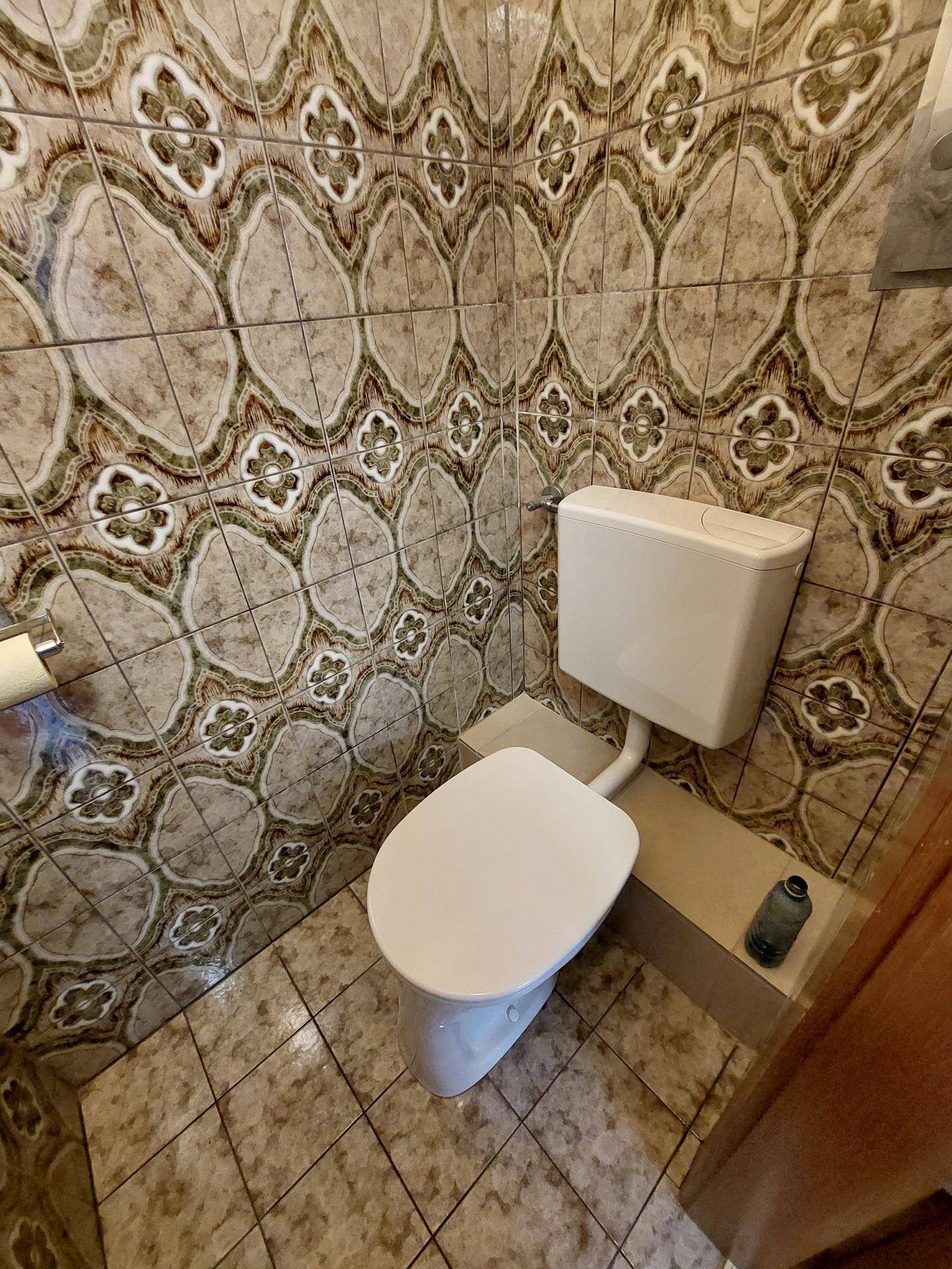 Gäste-WC mit gemusterten Fliesen an Wänden und Boden sowie einer Toilette.