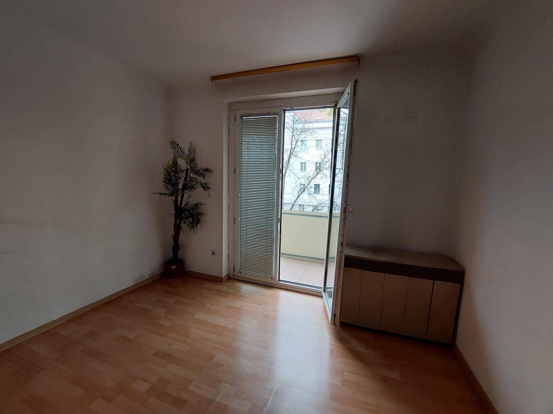 Schlafzimmer mit Parkettboden, Balkonzugang und einem kleinen Beistellschrank.