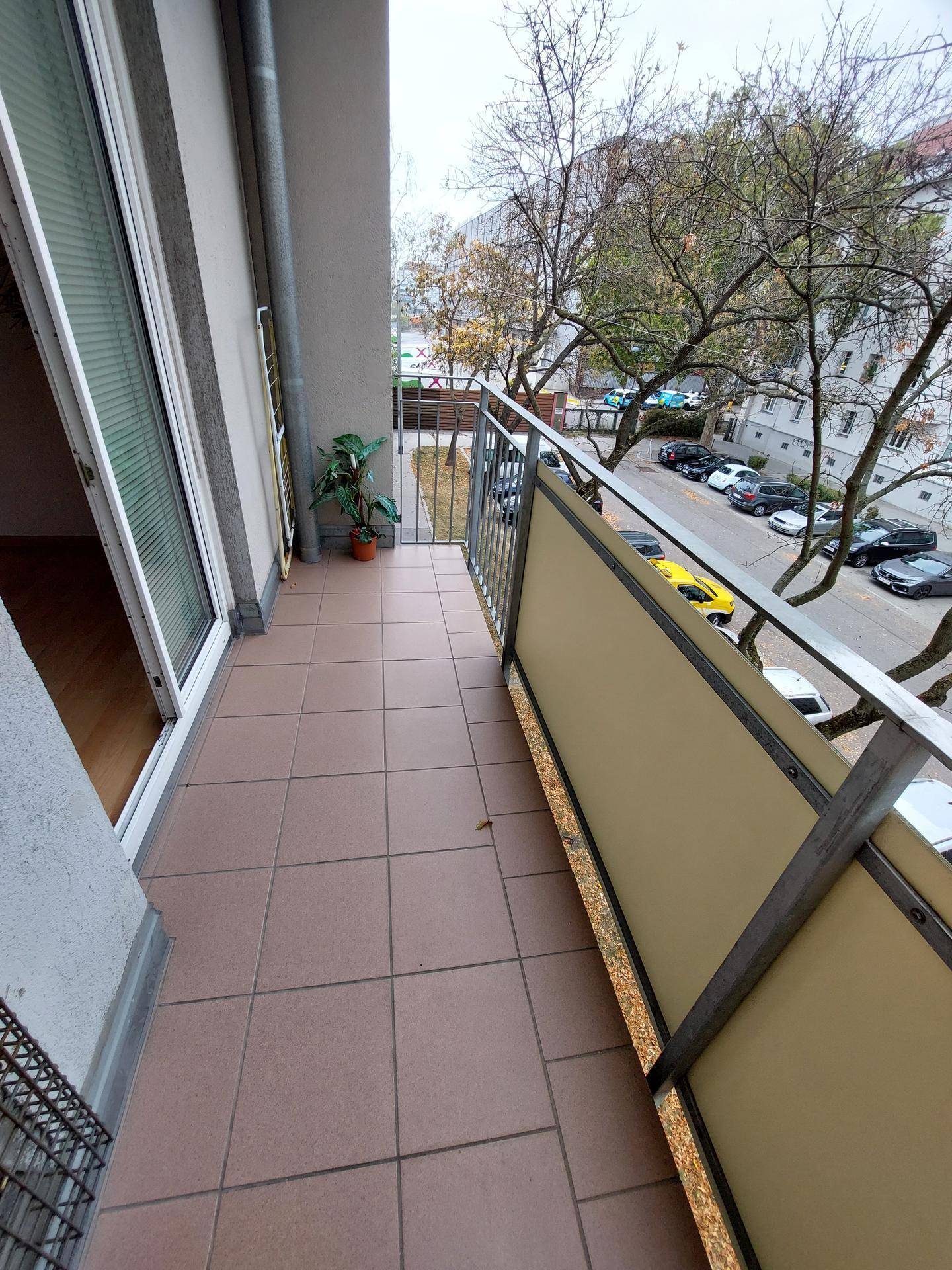 Balkon mit Fliesenboden und Blick auf die Straße und Bäume.
