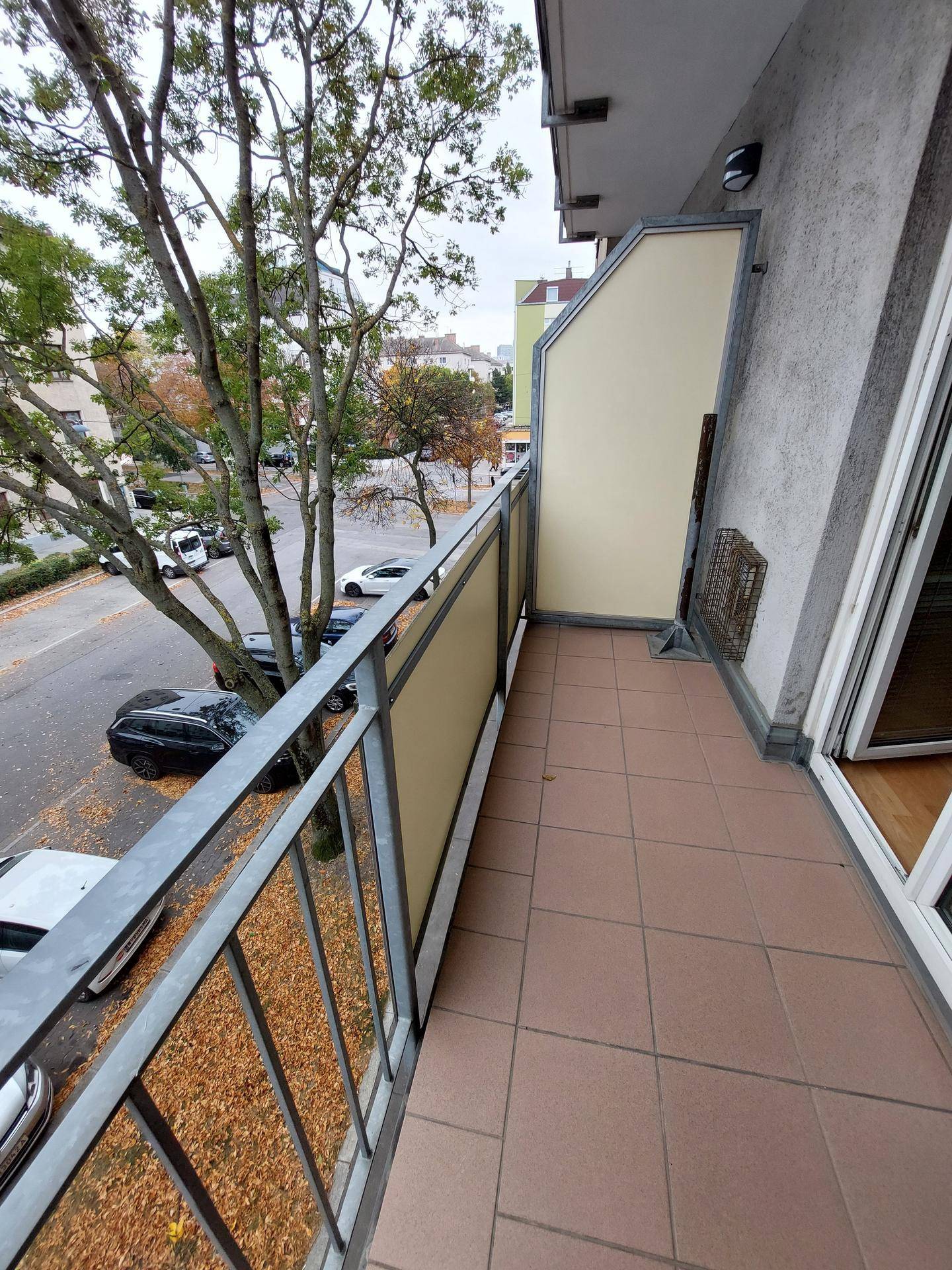 Balkon mit Fliesenboden und Blick auf die Straße und Bäume.