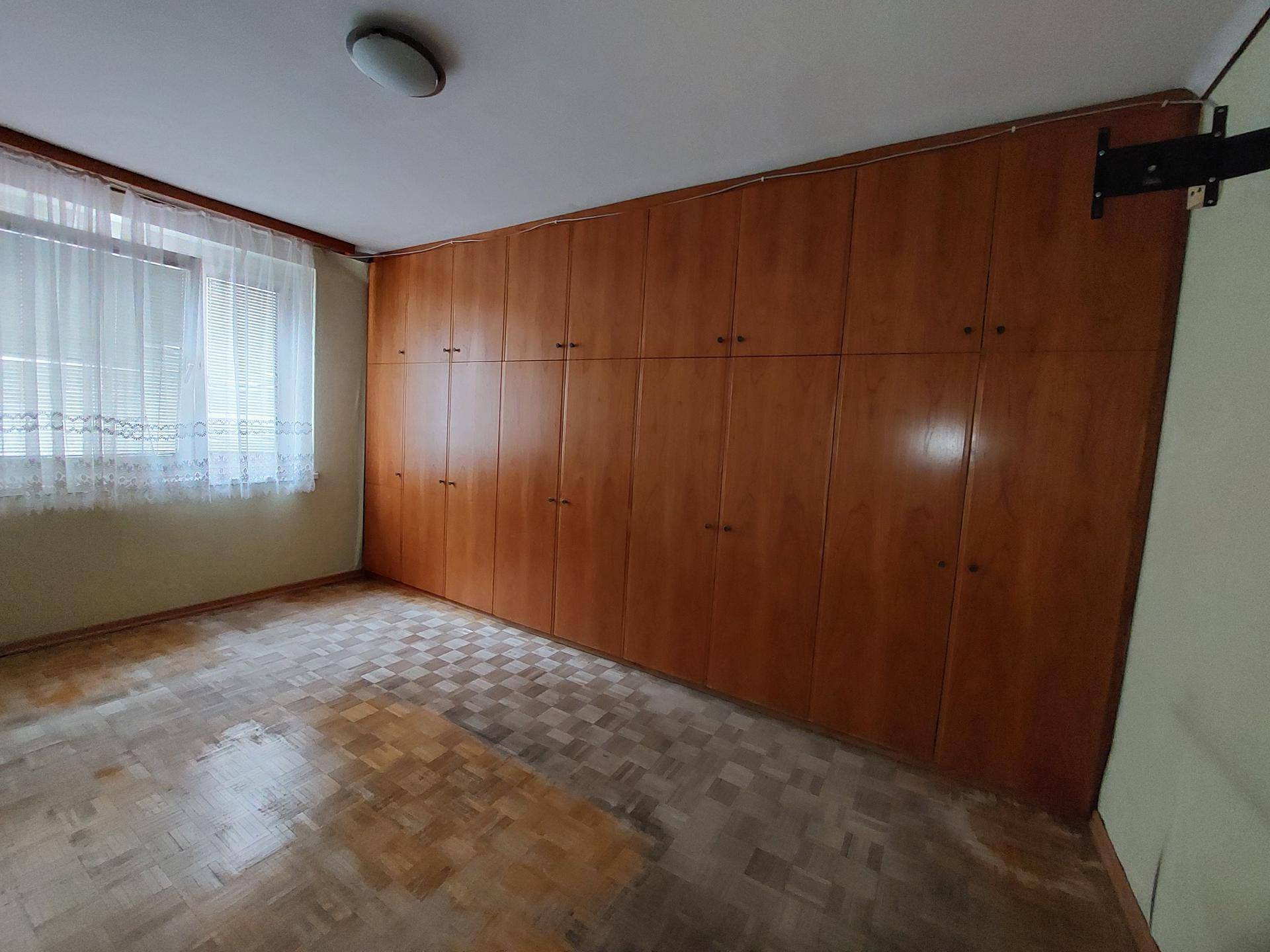 Schlafzimmer mit Einbauschränken, Parkettboden und Fenster mit Vorhängen.