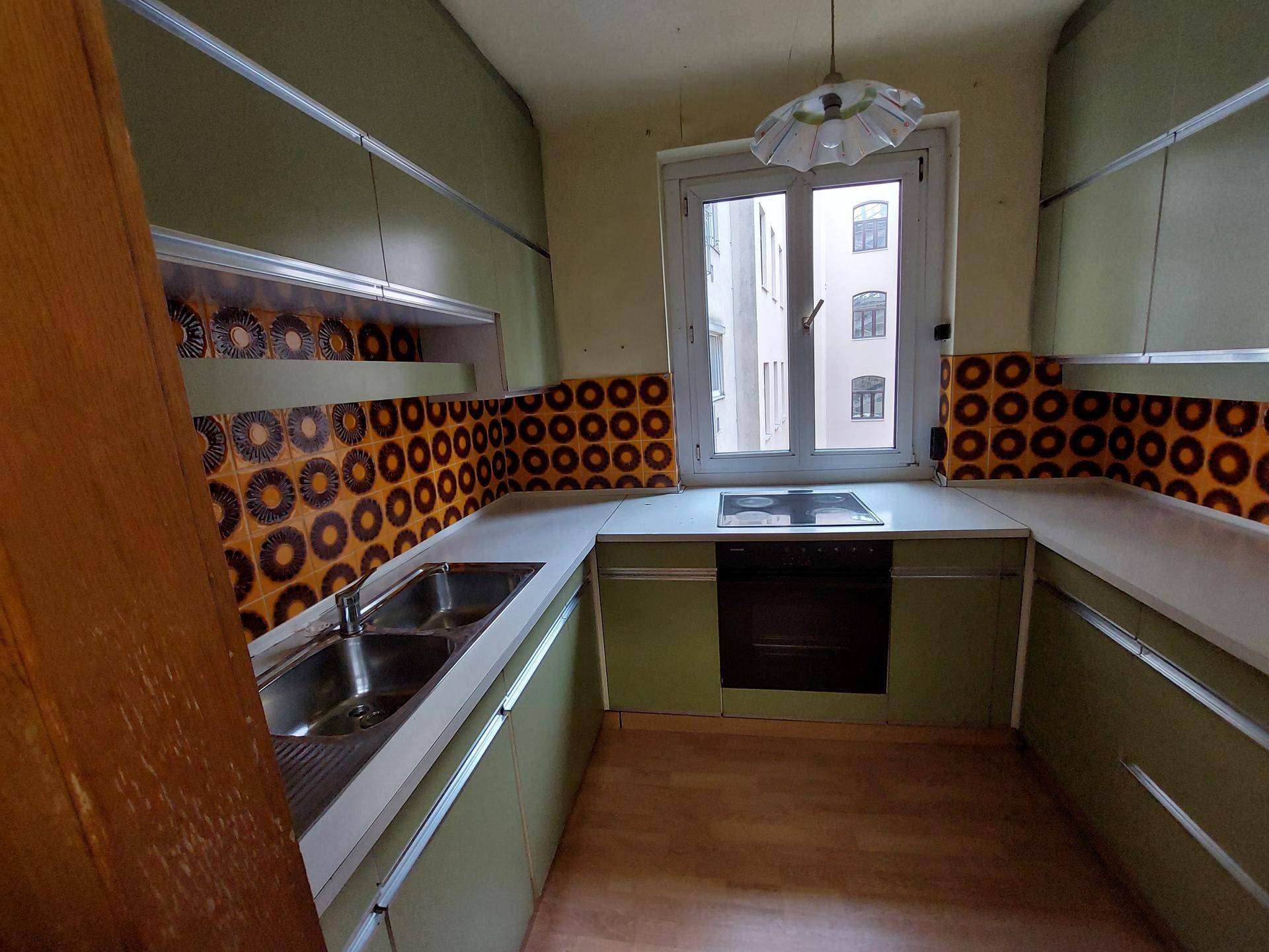 Küche im 70er-Jahre-Stil mit grünen Schränken, gemusterten Fliesen und Fenster.