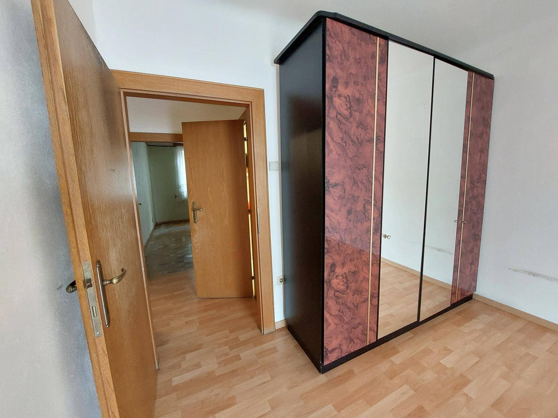 Schlafzimmer mit Parkettboden und einem großen Kleiderschrank mit Spiegeltüren.