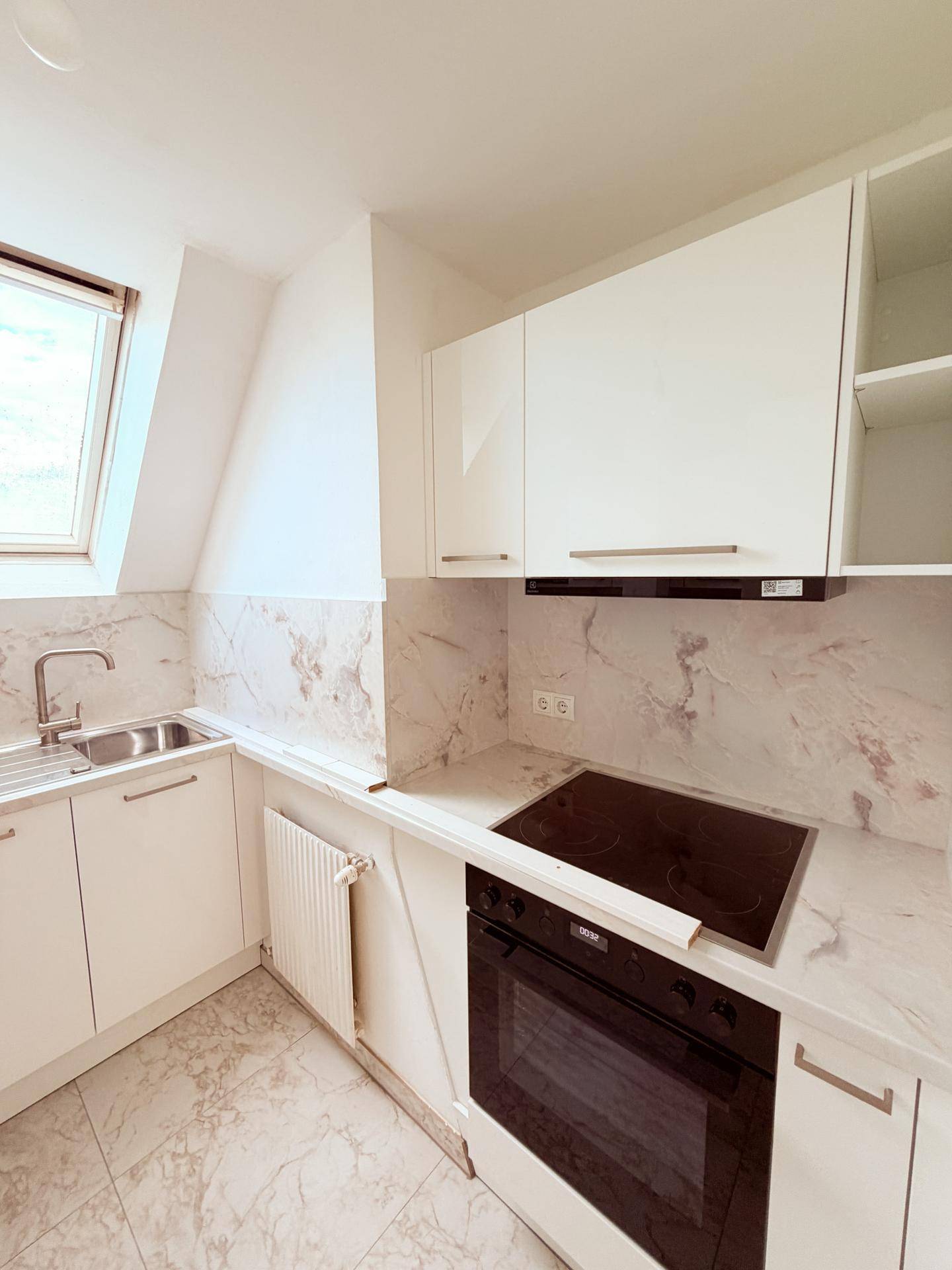 Moderne Küche mit weißen Schränken, Marmoroptik-Arbeitsplatten und Dachfenster für viel Licht.
