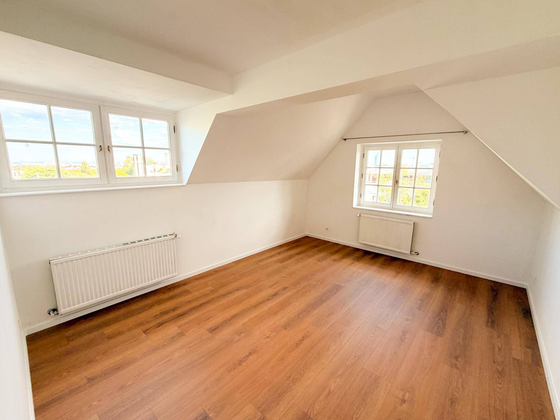 Helles Schlafzimmer im Dachgeschoss mit Holzboden, Dachschrägen und zwei Fenstern.
