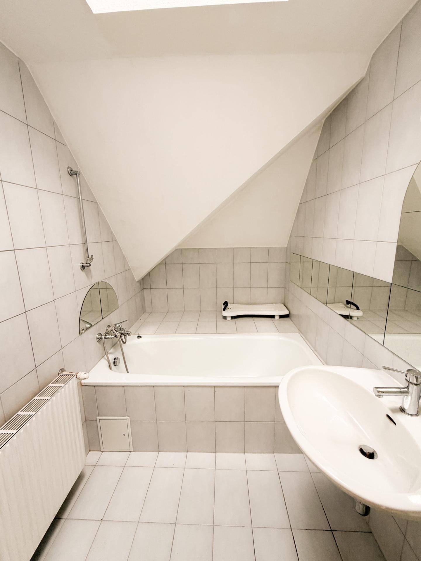 Helles Badezimmer mit Badewanne, Fliesenboden und schrägen Wänden im Dachgeschoss.