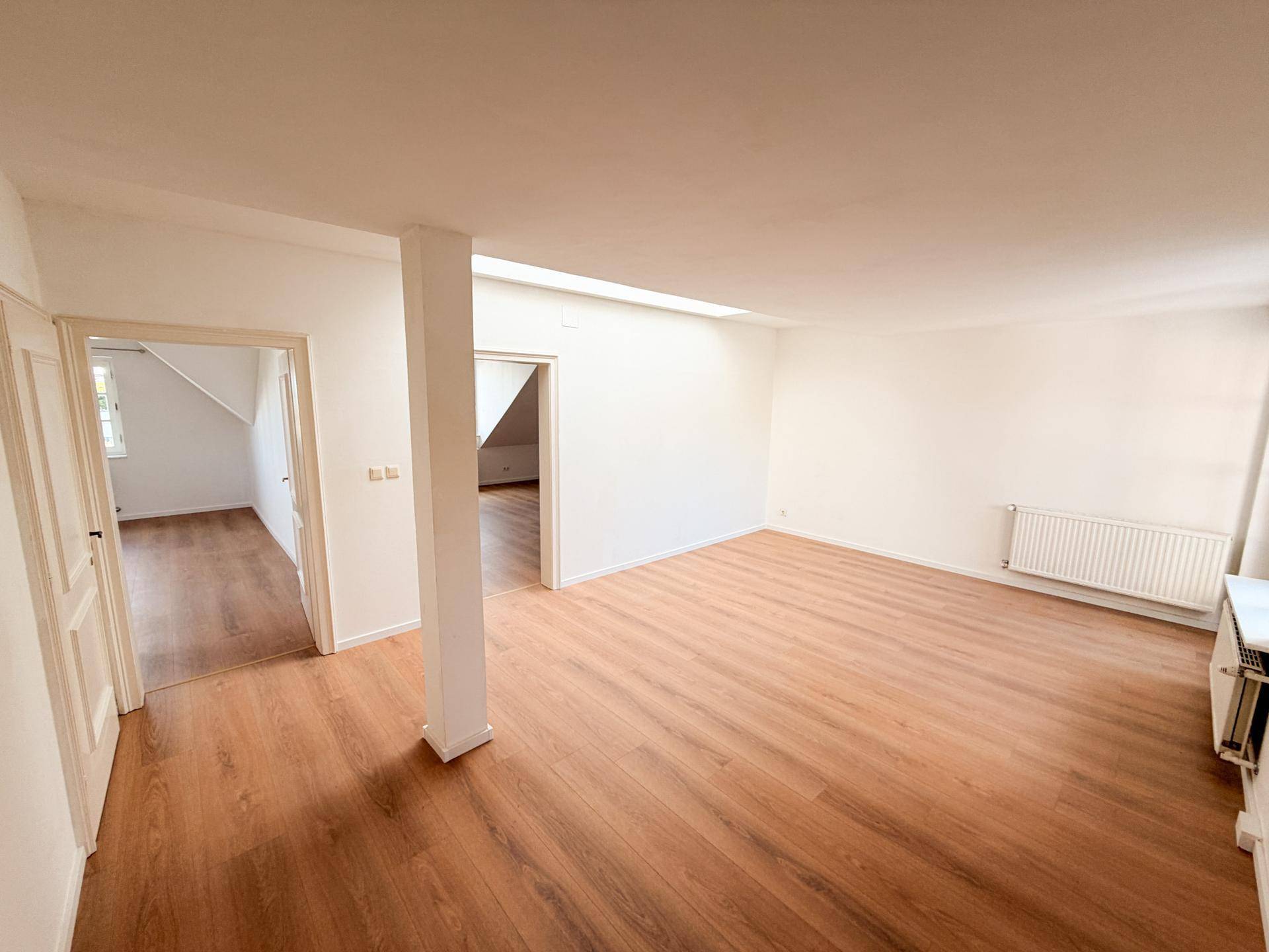 Großer, heller Raum mit Holzboden und Zugang zu weiteren Zimmern im Dachgeschoss.
