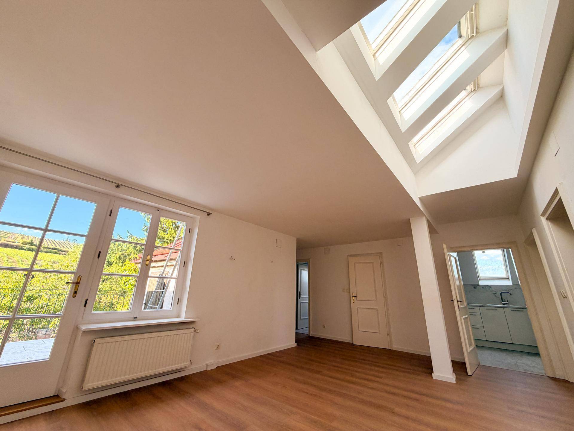 Großzügiges Wohnzimmer mit Holzboden, hohen Decken und vielen Fenstern für Tageslicht.
