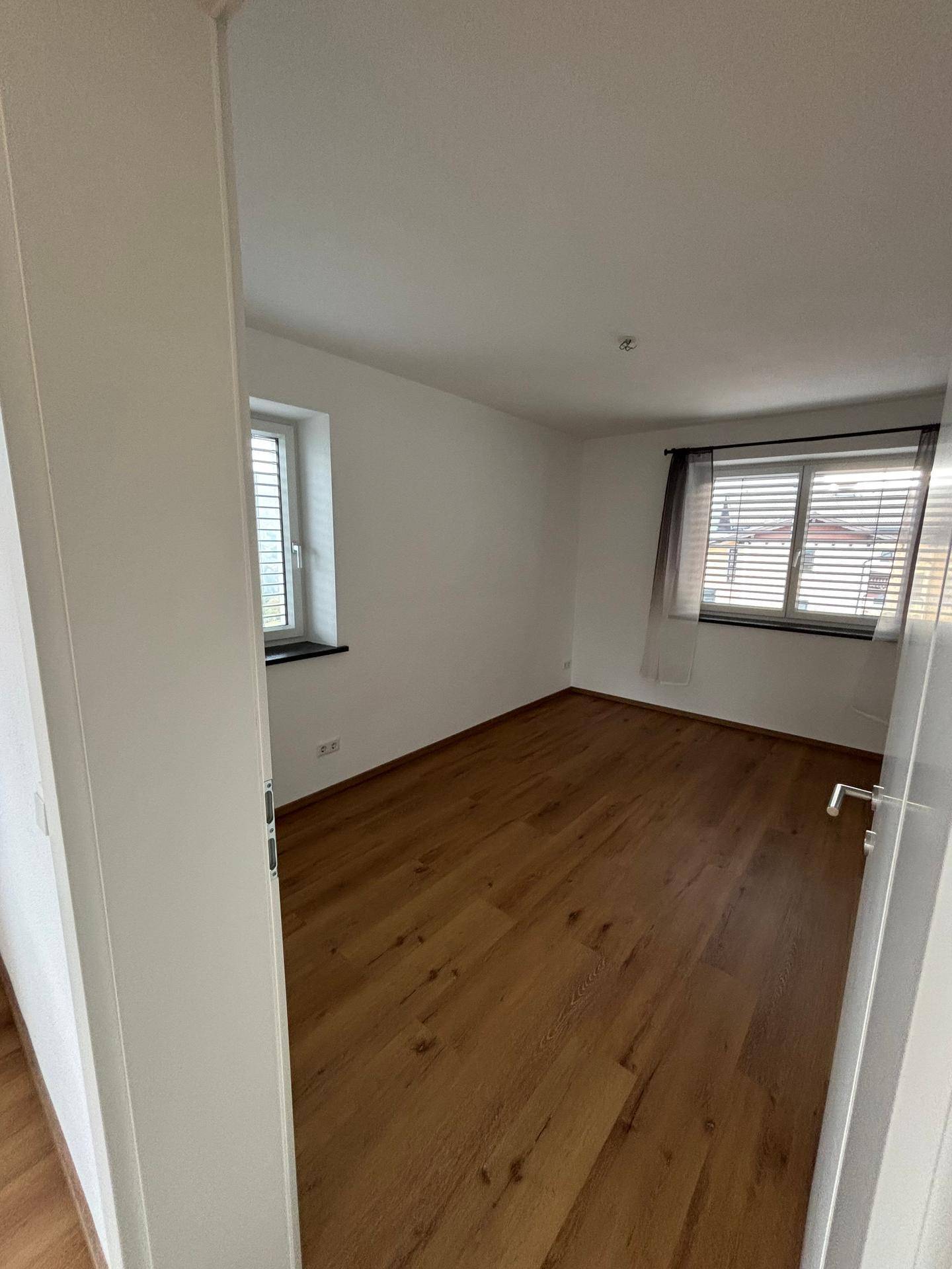 Helles Schlafzimmer mit Holzboden und zwei Fenstern, die viel Tageslicht hereinlassen.