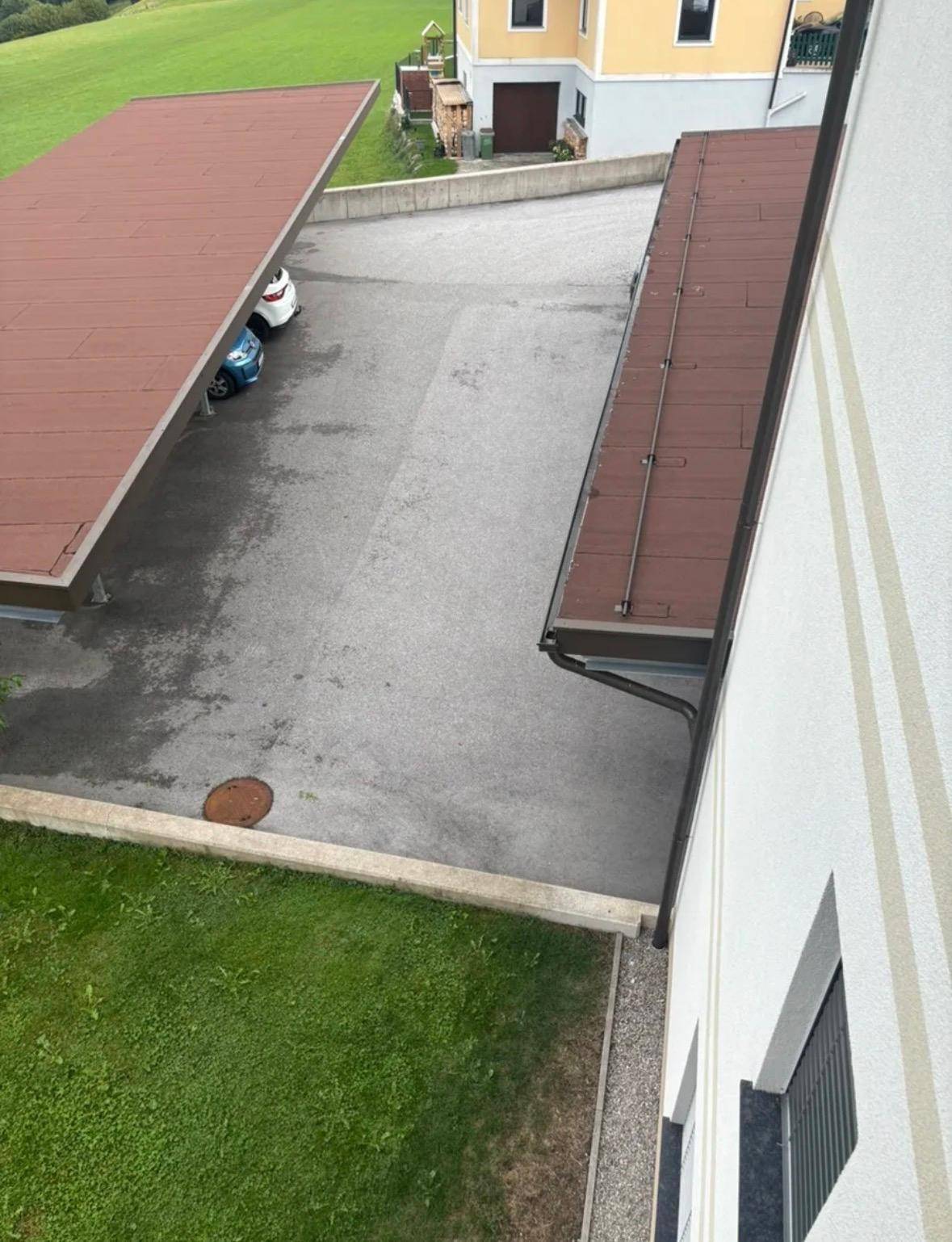 Außenbereich mit Parkplätzen unter einem Carport und angrenzender Grünfläche.