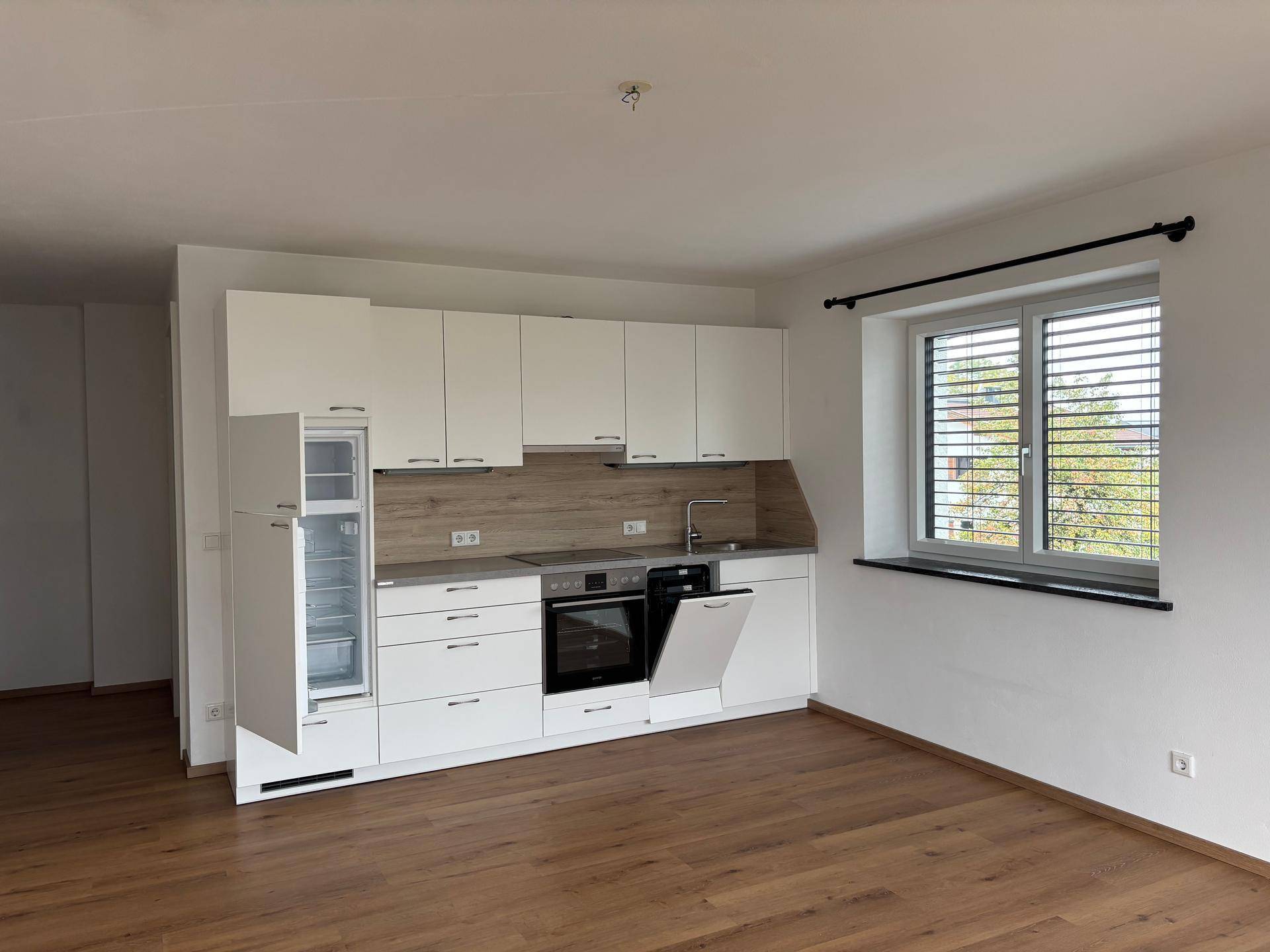Moderne Einbauküche mit weißen Schränken, integrierten Geräten und Holzboden in offenem Raum.
