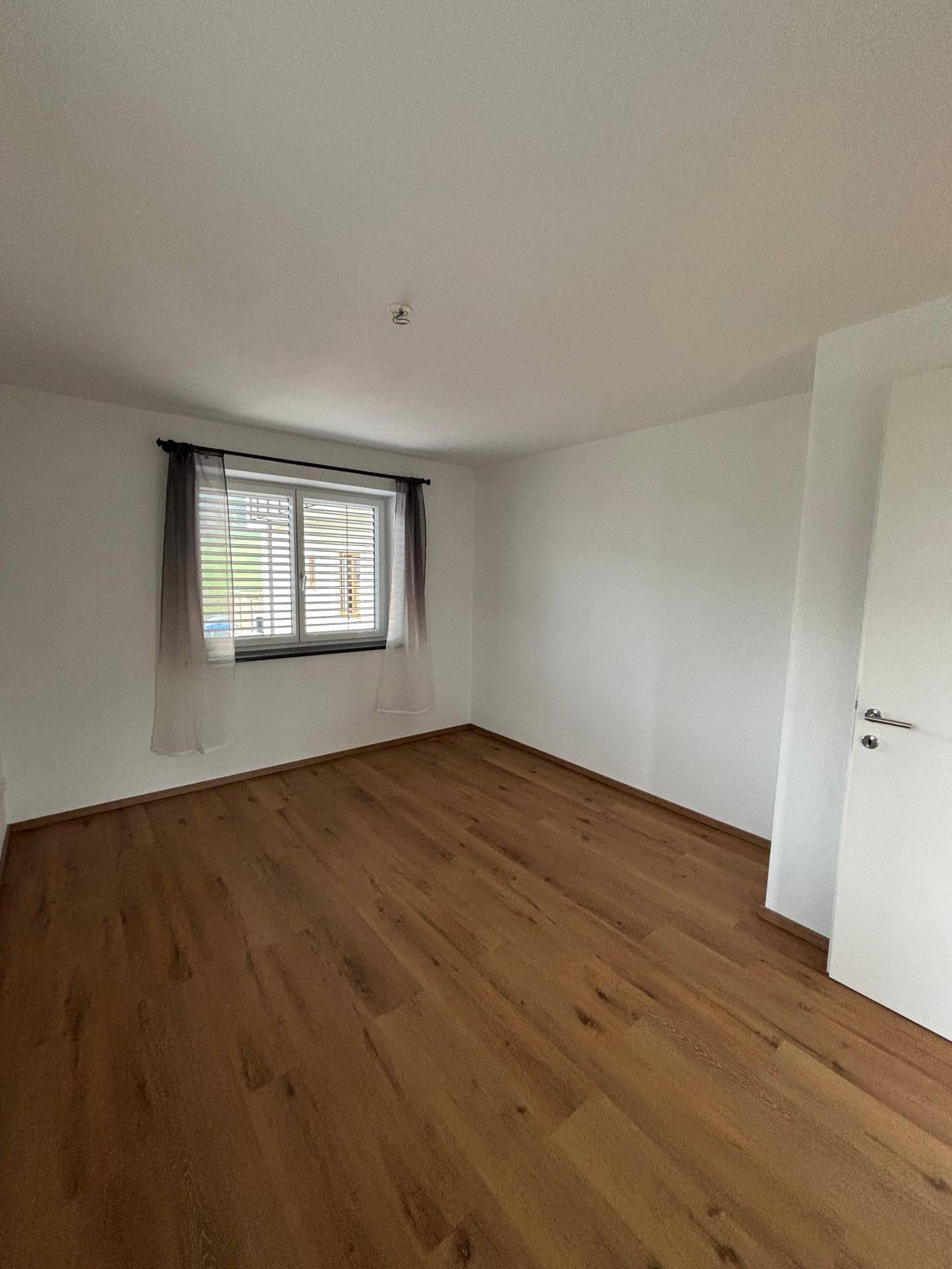 Geräumiges Schlafzimmer mit warmem Holzboden und großem Fenster für eine helle Atmosphäre.