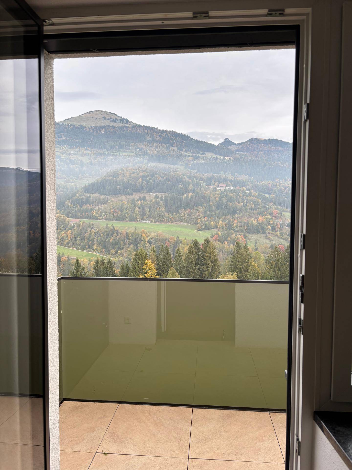 Geräumiger Balkon mit Fliesenboden und weitem Blick über bewaldete Hügel und Berge.