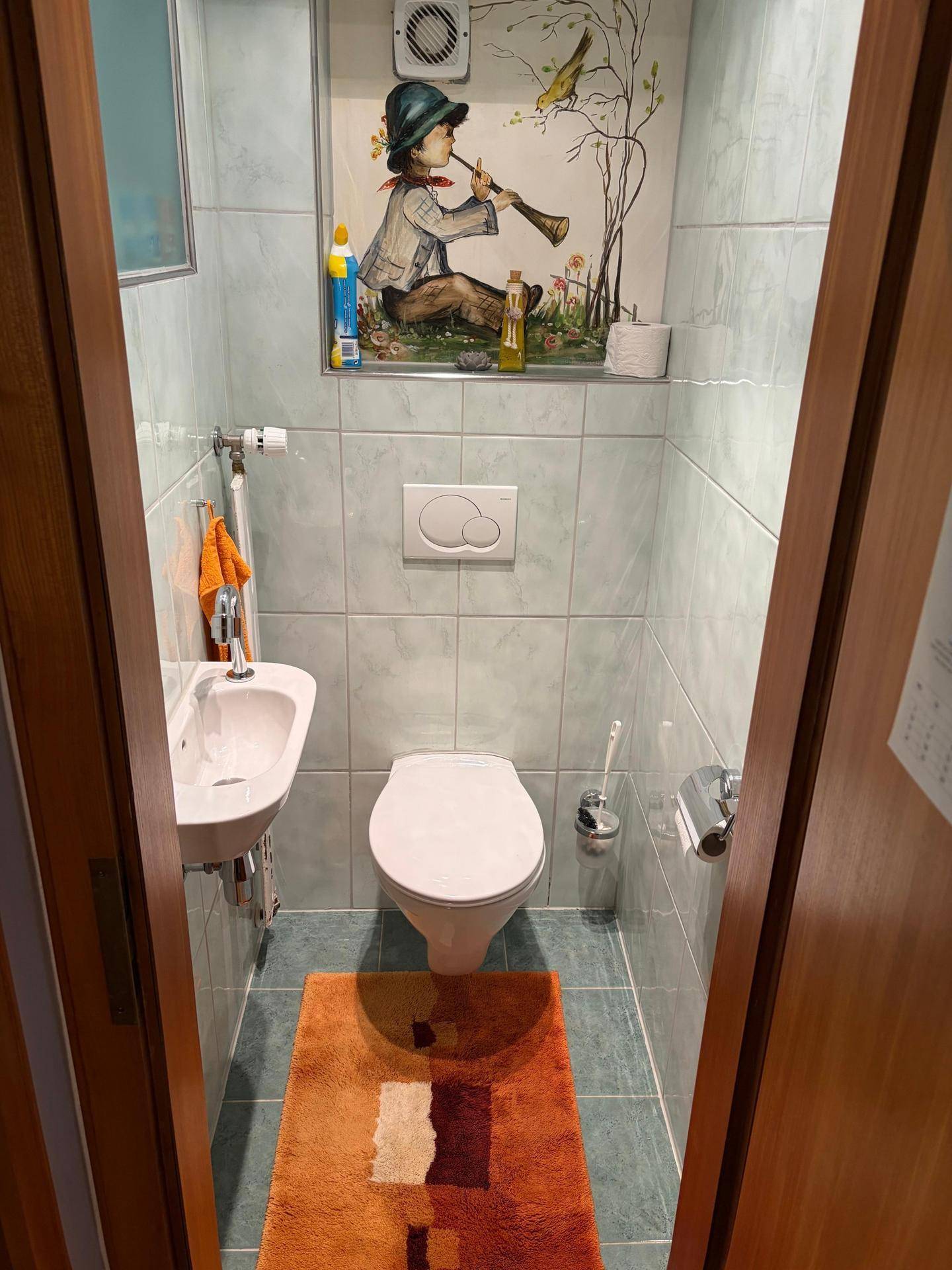 Kleines Gäste-WC mit Wand-WC, Handwaschbecken und Fliesenboden.