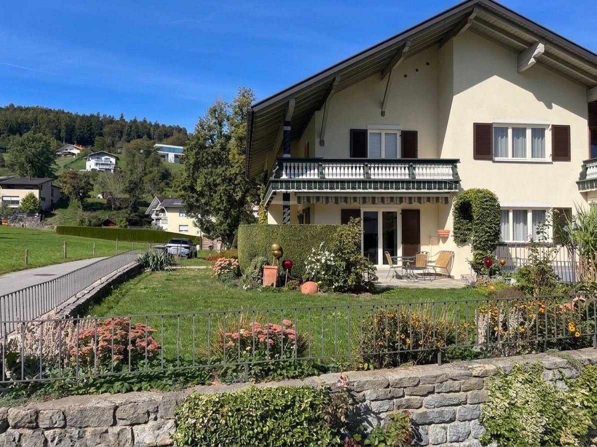 Vorderansicht des Hauses mit Terrasse, Garten und Blick auf die grüne Umgebung.
