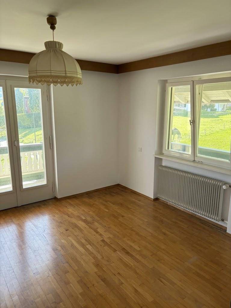 Leeres Zimmer mit Parkettboden, Balkonzugang und Blick auf die Landschaft.